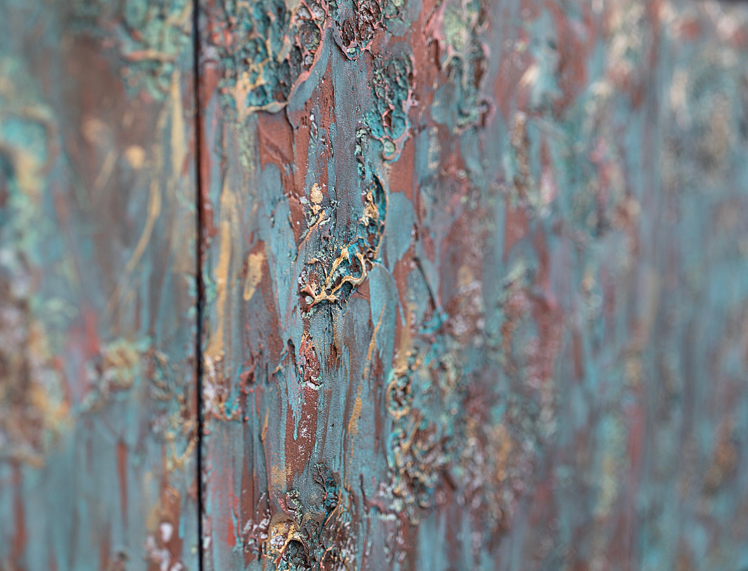 Close-up of a textured art piece featuring a mix of turquoise, gold, and reddish-brown hues. The paint appears layered and uneven, creating a rugged surface with intricate patterns.