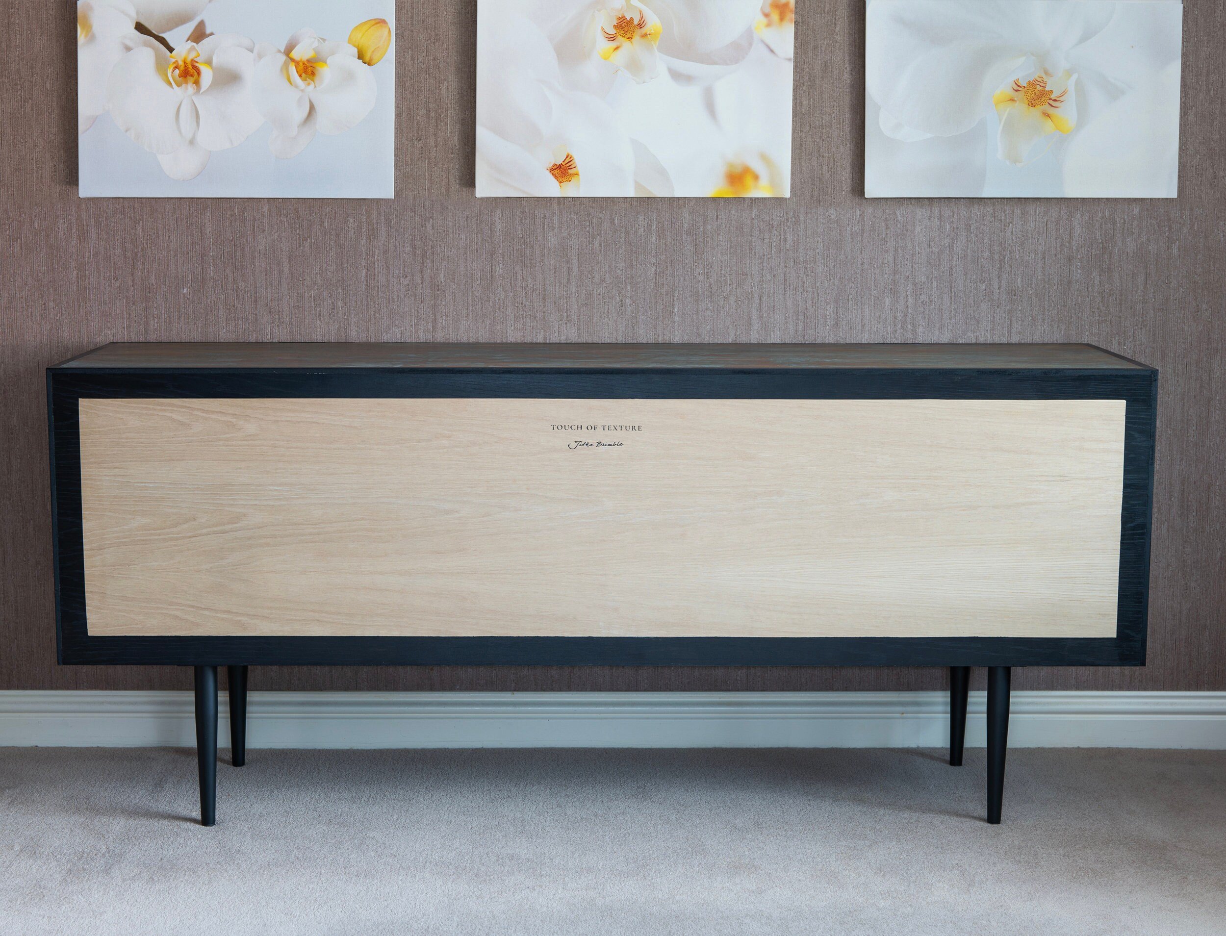 A custom-made modern wooden sideboard with black legs and trim stands against a textured wall.