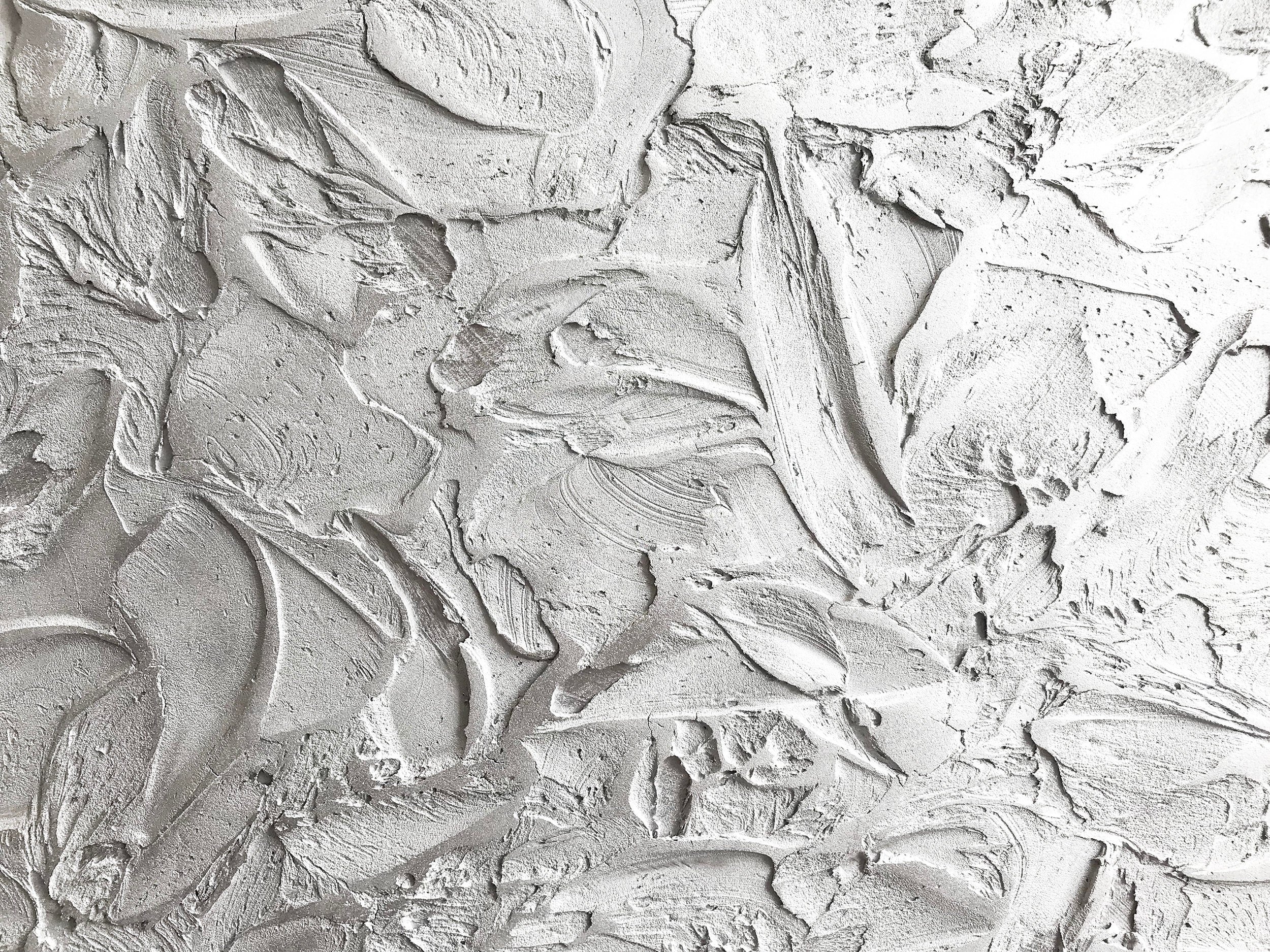 A close-up of textured art reveals abstract, three-dimensional patterns in shades of light gray. The surface appears rough and uneven.