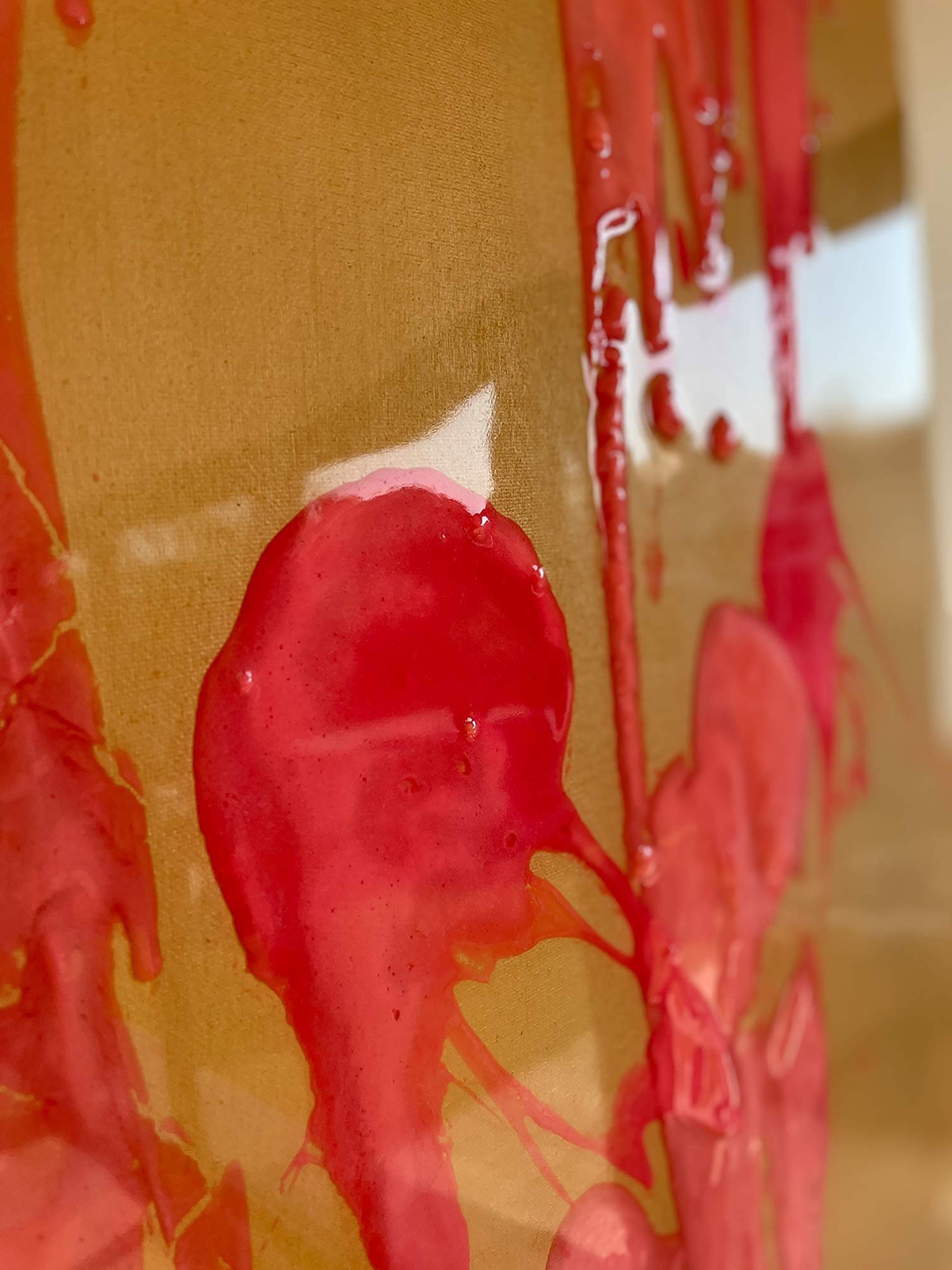 Close-up of an abstract painting with streaks and drips of glossy pink paint on a mustard-colored background. The texture is thick and layered, casting subtle shadows on the surface.