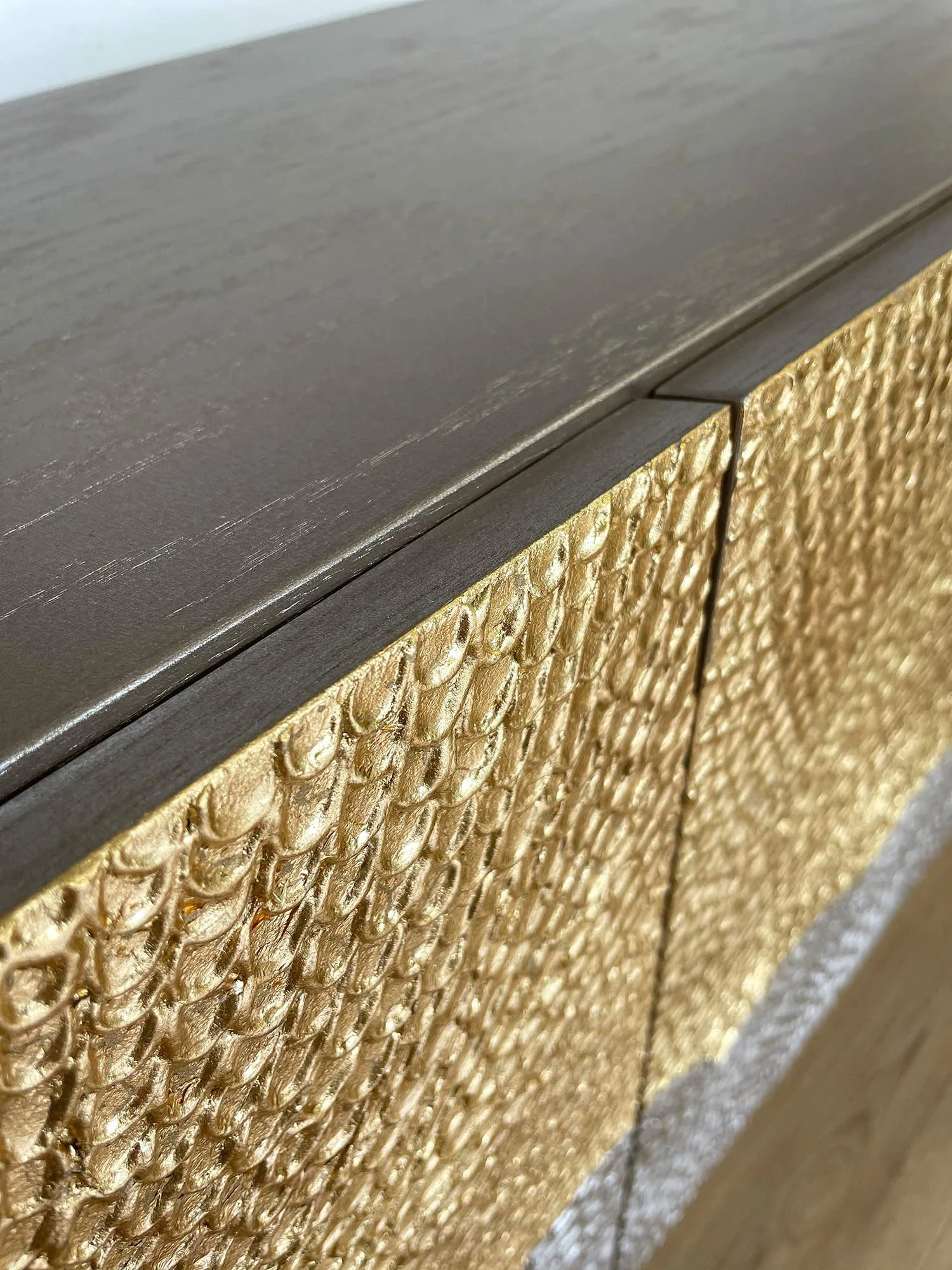 Close up on a detail of a statement gold leaf credenza, showcasing a mitred style doors, that are textured and gilded.