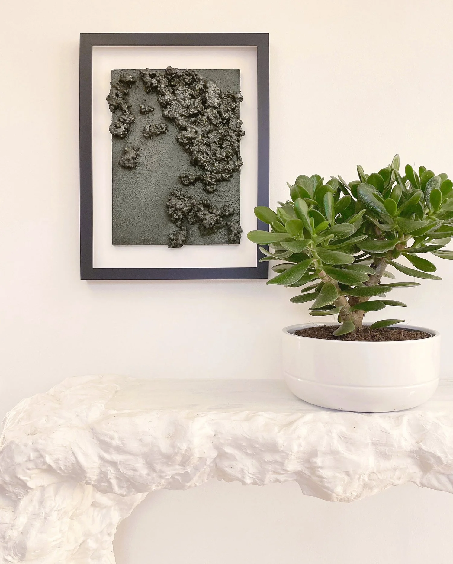 An abstract accent wall art with dark, bumpy texture, where small, rounded clusters of recycled waste material create a rugged, almost volcanic look against a smooth backdrop.