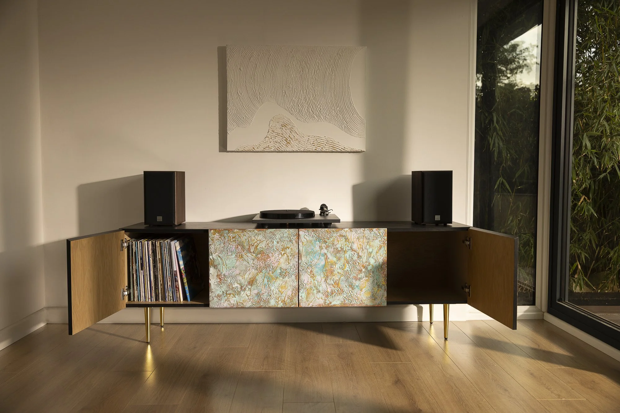 A cosy room with a large sideboard featuring four colourful, textured doors. Two of the doors are open, revealing a record storage.
