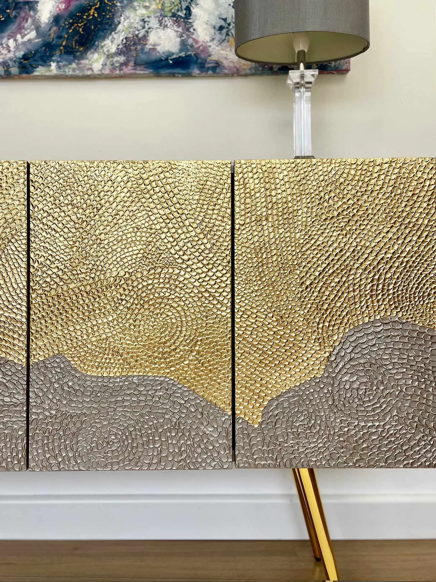 Statement gold leaf credenza styled in a modern luxury living room with abstract wall art and designer lamps.