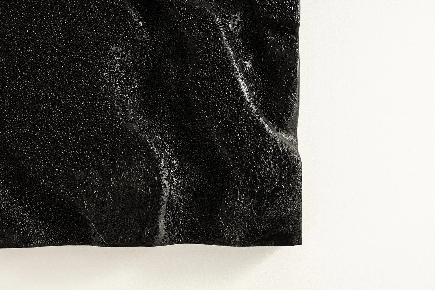 Close-up detail of the rough, granular and wavy black texture on the "Obsidian Tide" wall sculpture.