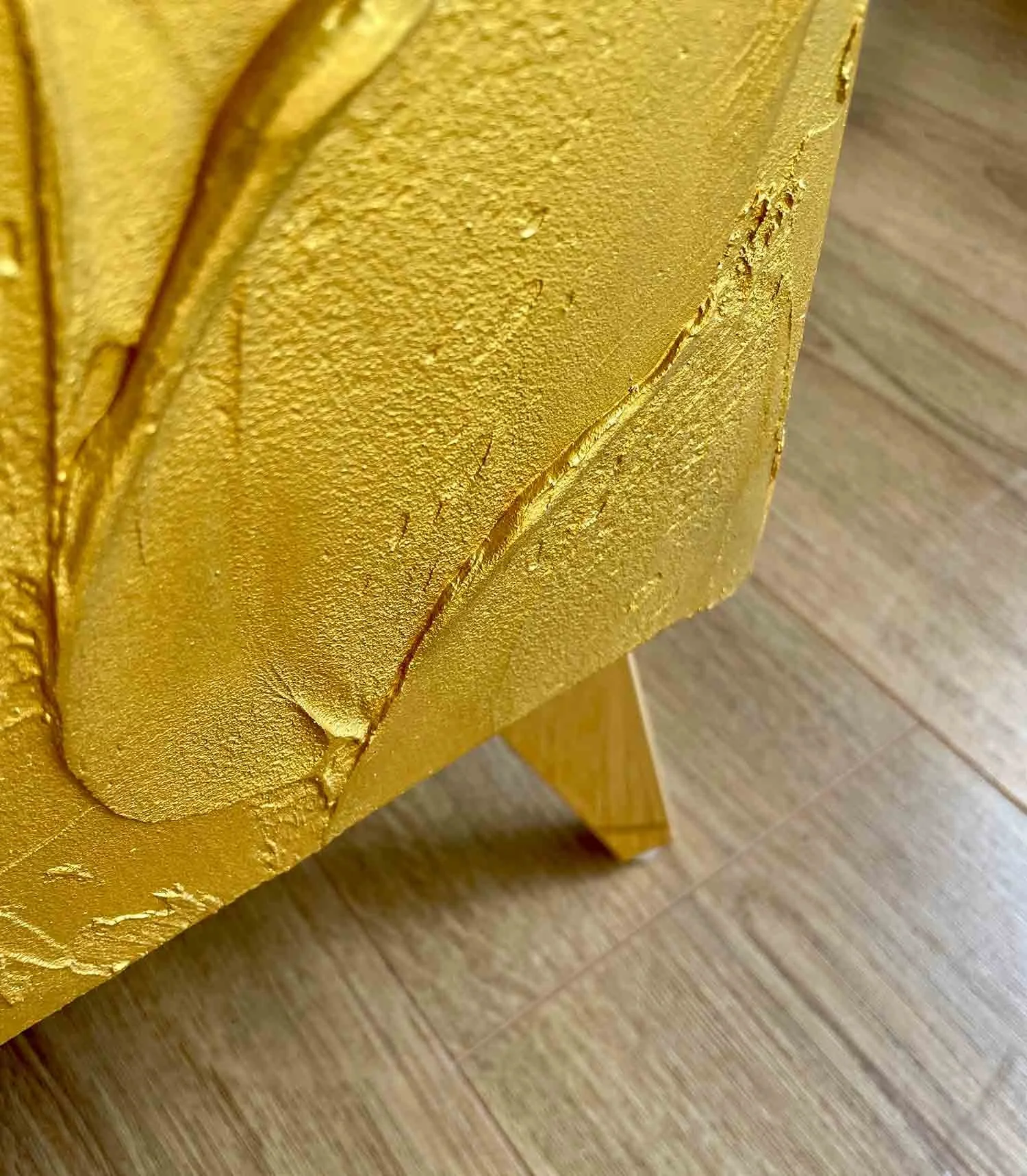 Close-up shot of the handcrafted botanical leaf texture on a shimmering metallic gold background.