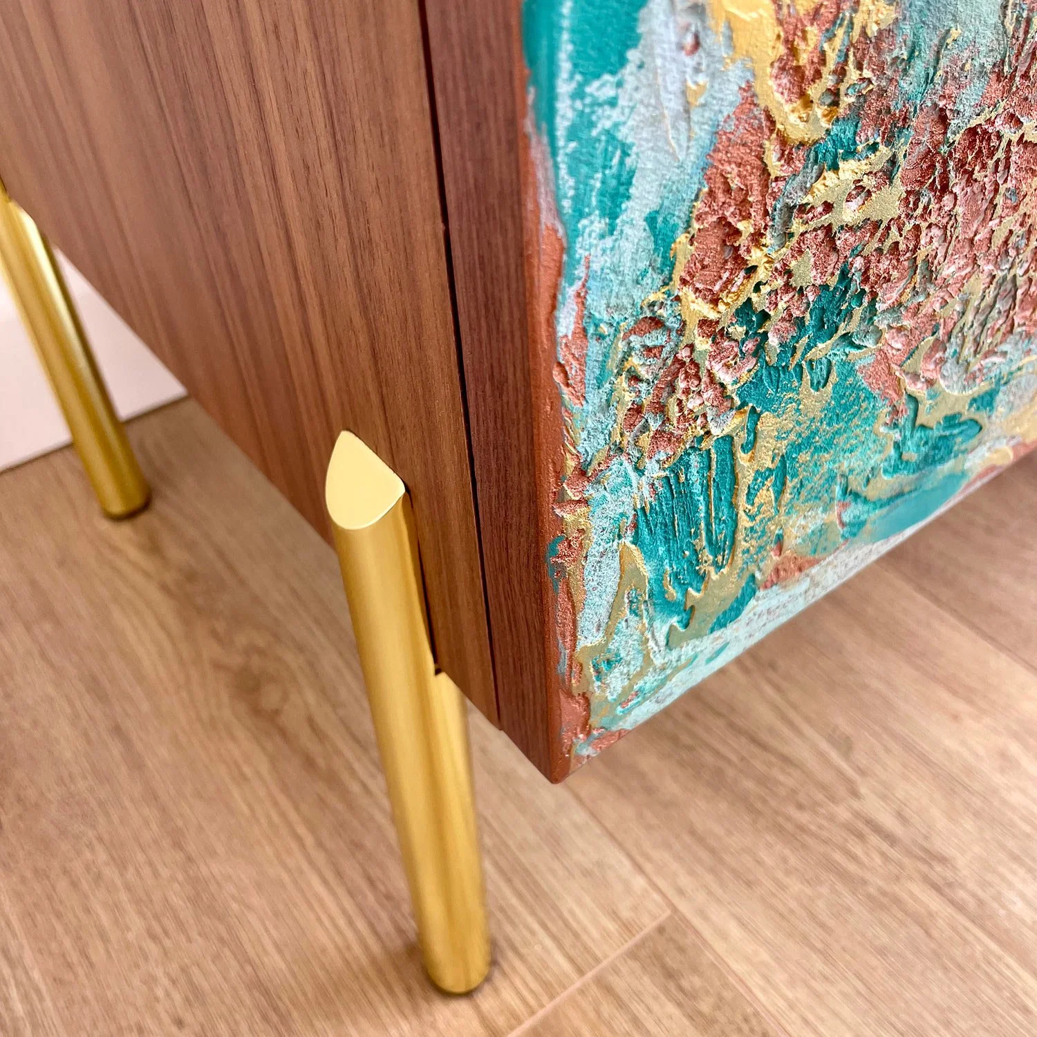 Close-up of a sideboard corner with wooden sides and colourful textured doors, featuring a visible gold straight foot.