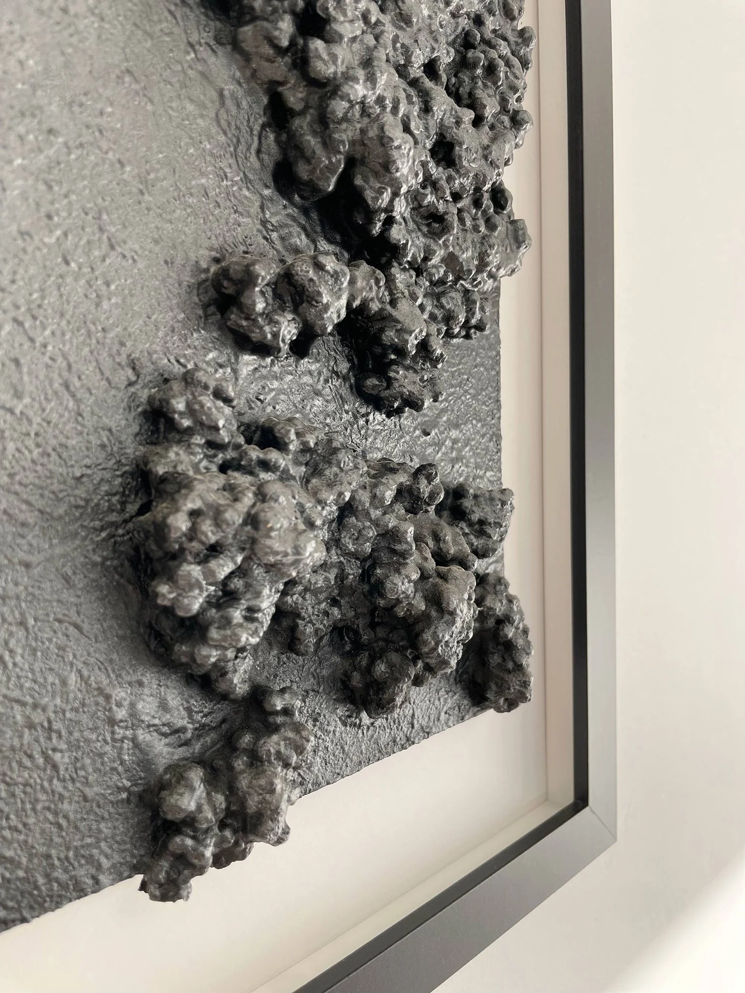 Close-up view of the three-dimensional texture of the recycled waste wall art, with glossy, black formations that resemble hardened lava, contrasting with the rough, matte background.