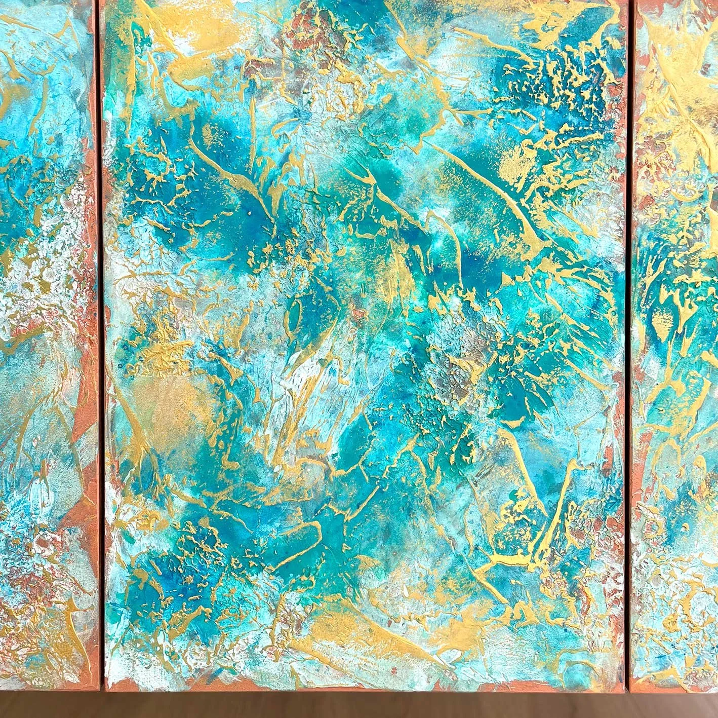 Close-up of a sideboard door with gold shimmer markings over a colourful mix of turquoise and blue tones on a textured surface.