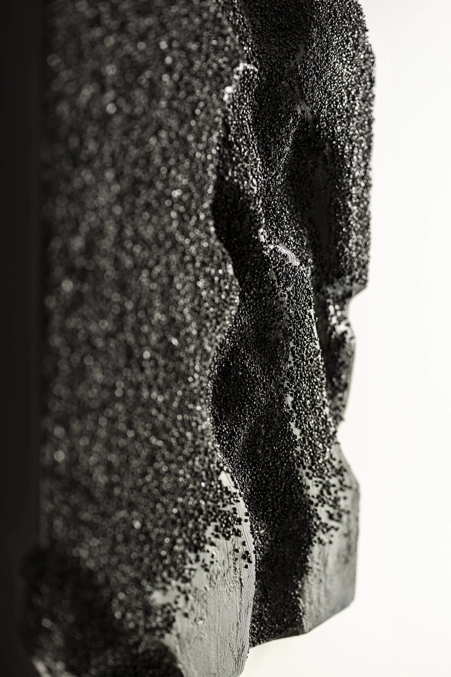 Close-up of the flowing, uneven, lava-like surface of the black high-relief sculpture.