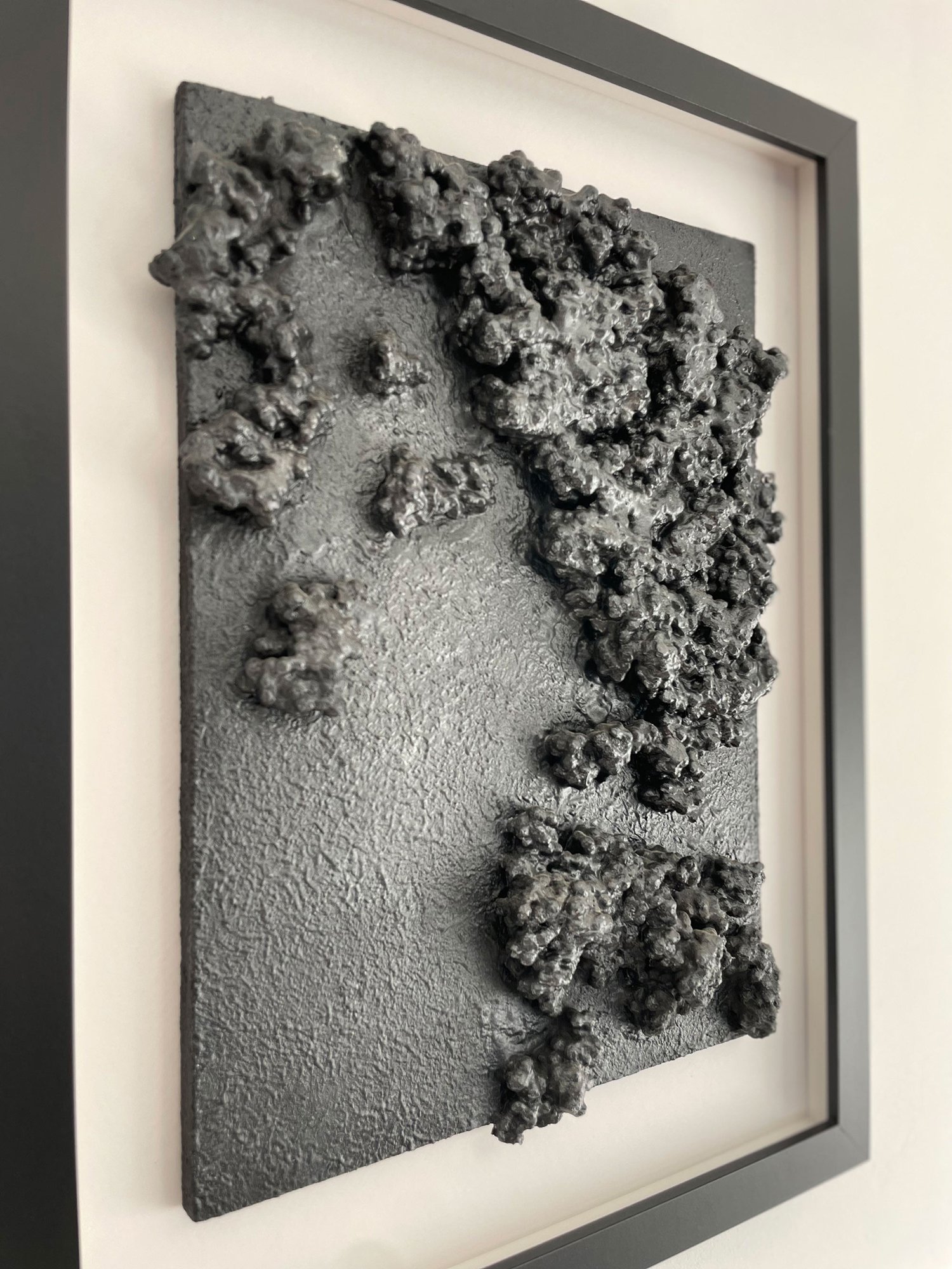 A side perspective of the wall art showing the raised, glossy clusters of repurposed waste materials.