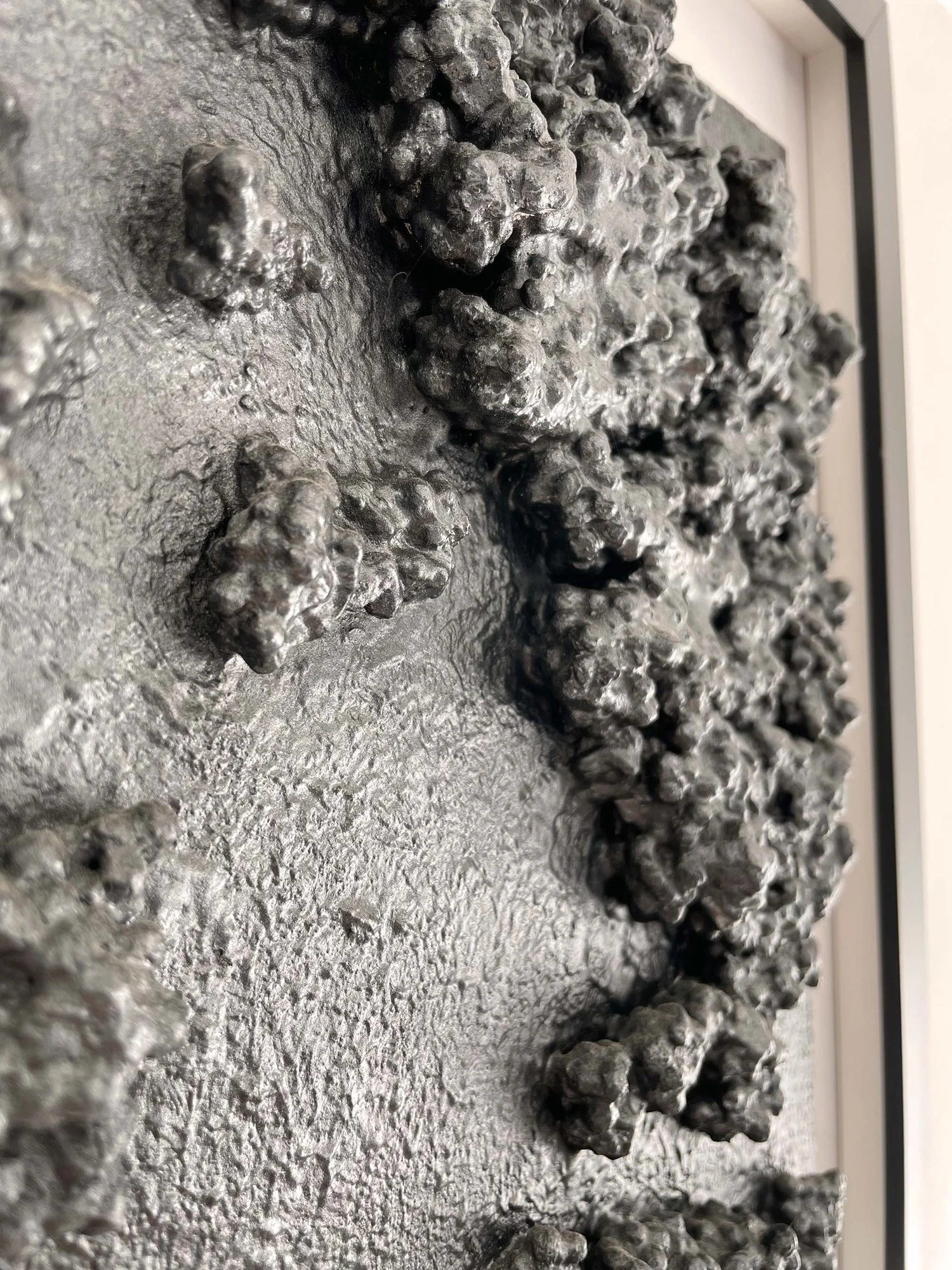 Close-up of the textured surface of the wall art, highlighting the dark, glossy clusters of recycled material that appear to form organic, irregular shapes.