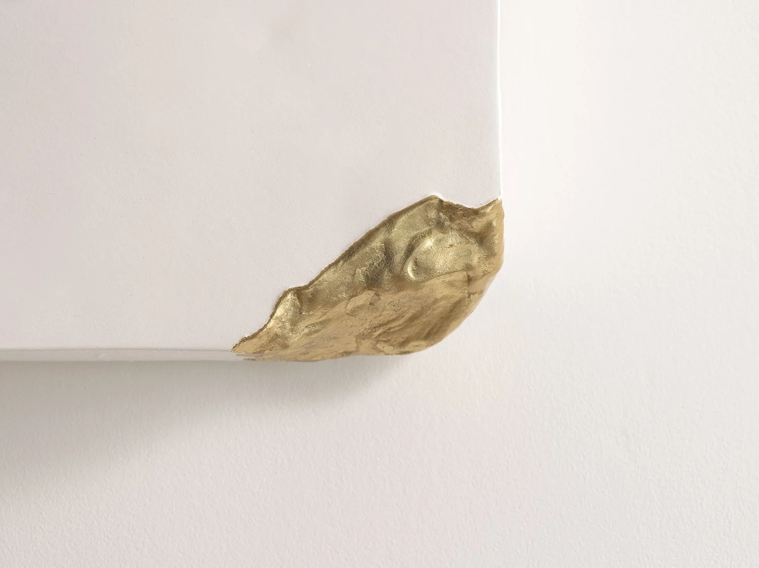 Close-up of the small, textured gold detail on the corner of the white sculptural artwork.