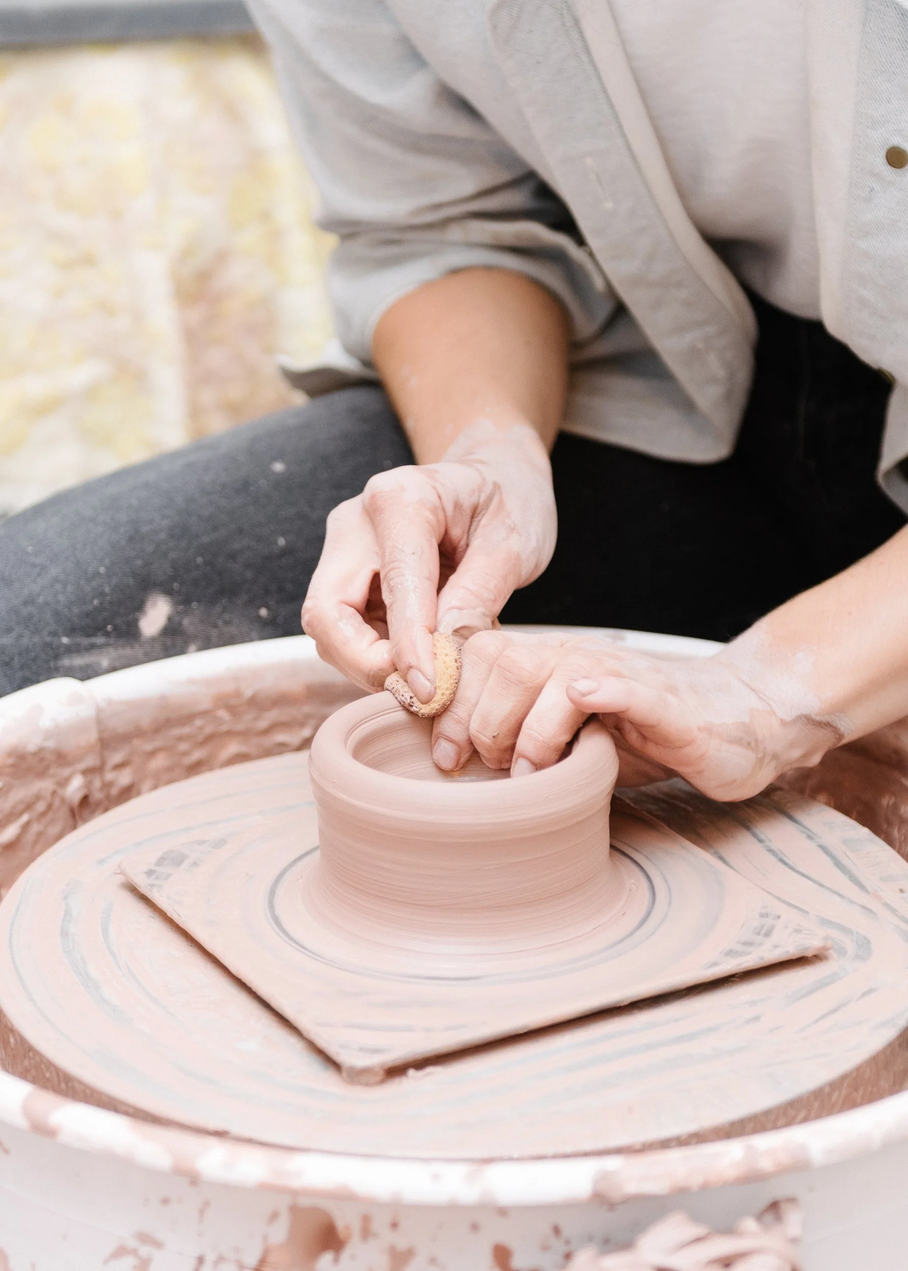 Two hands on a wheel, shaping brown clay.