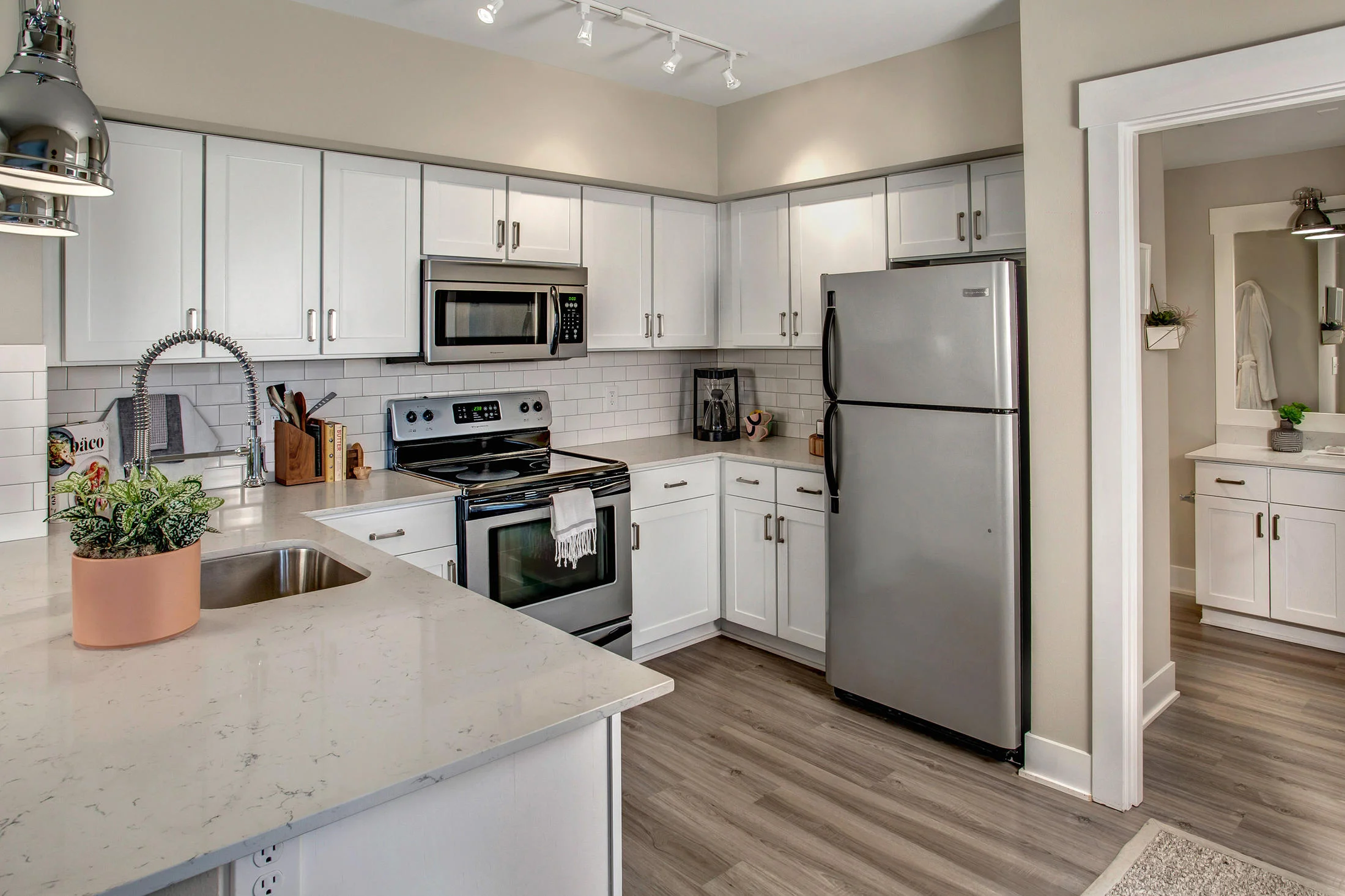 Modern kitchen with white cabinets, stainless steel appliances, a white countertop island, potted plant, and wooden flooring.