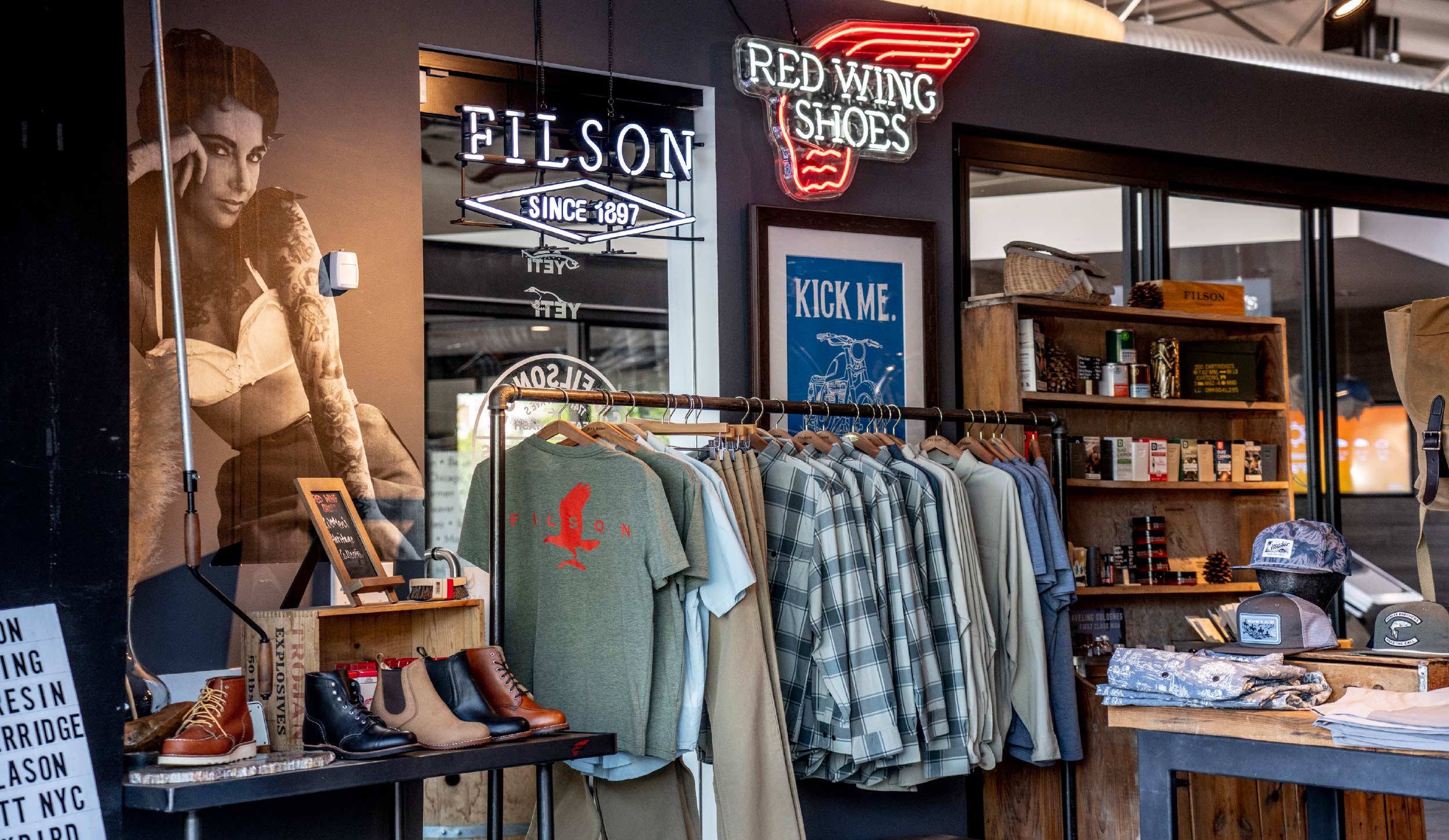 Display of shoes, clothing, and hats at a retail store with neon signs reading "Elson Since 1897" and "Red Wing Shoes".
