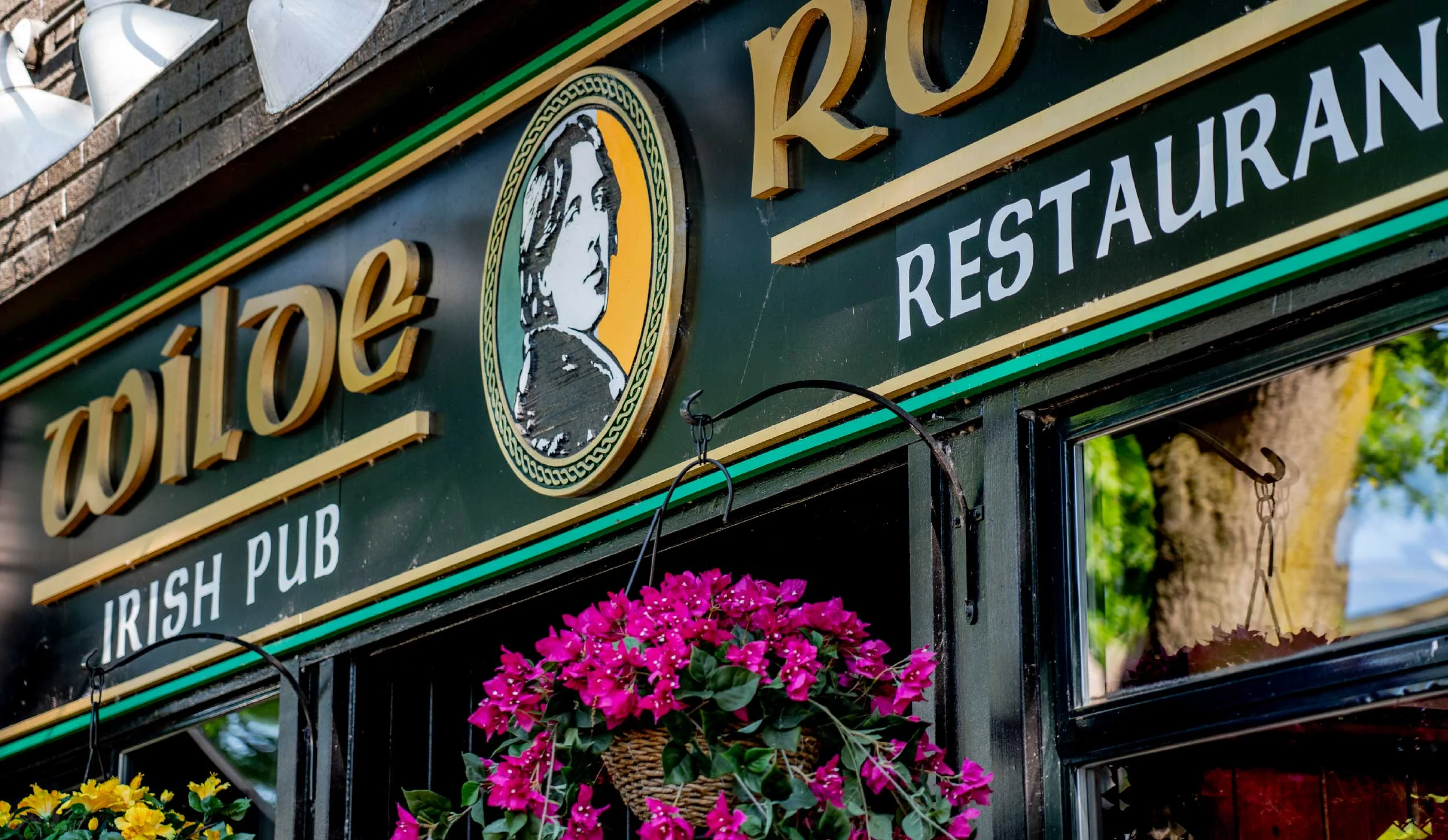 Sign outside an Irish pub, featuring a portrait of a woman in profile and hanging pink flowers.