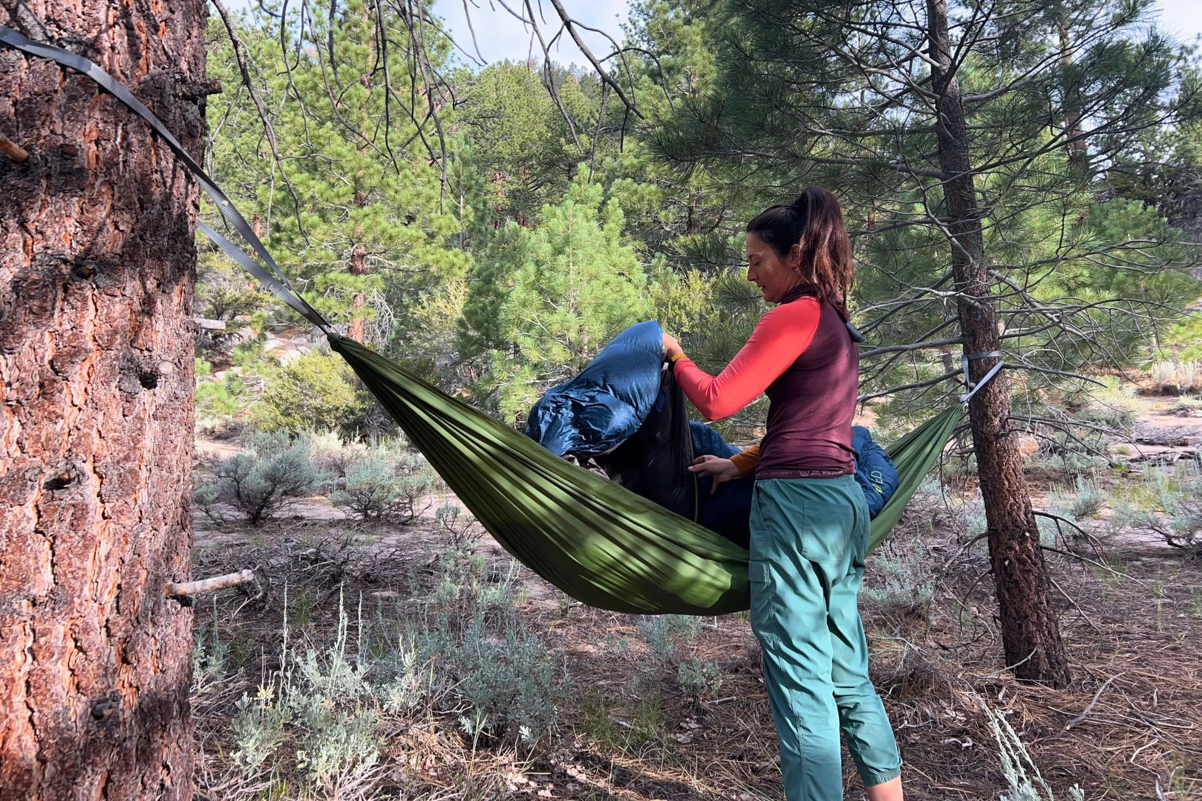 A woman holding the Exped Terra sleeping bag over a hammock in the trees.