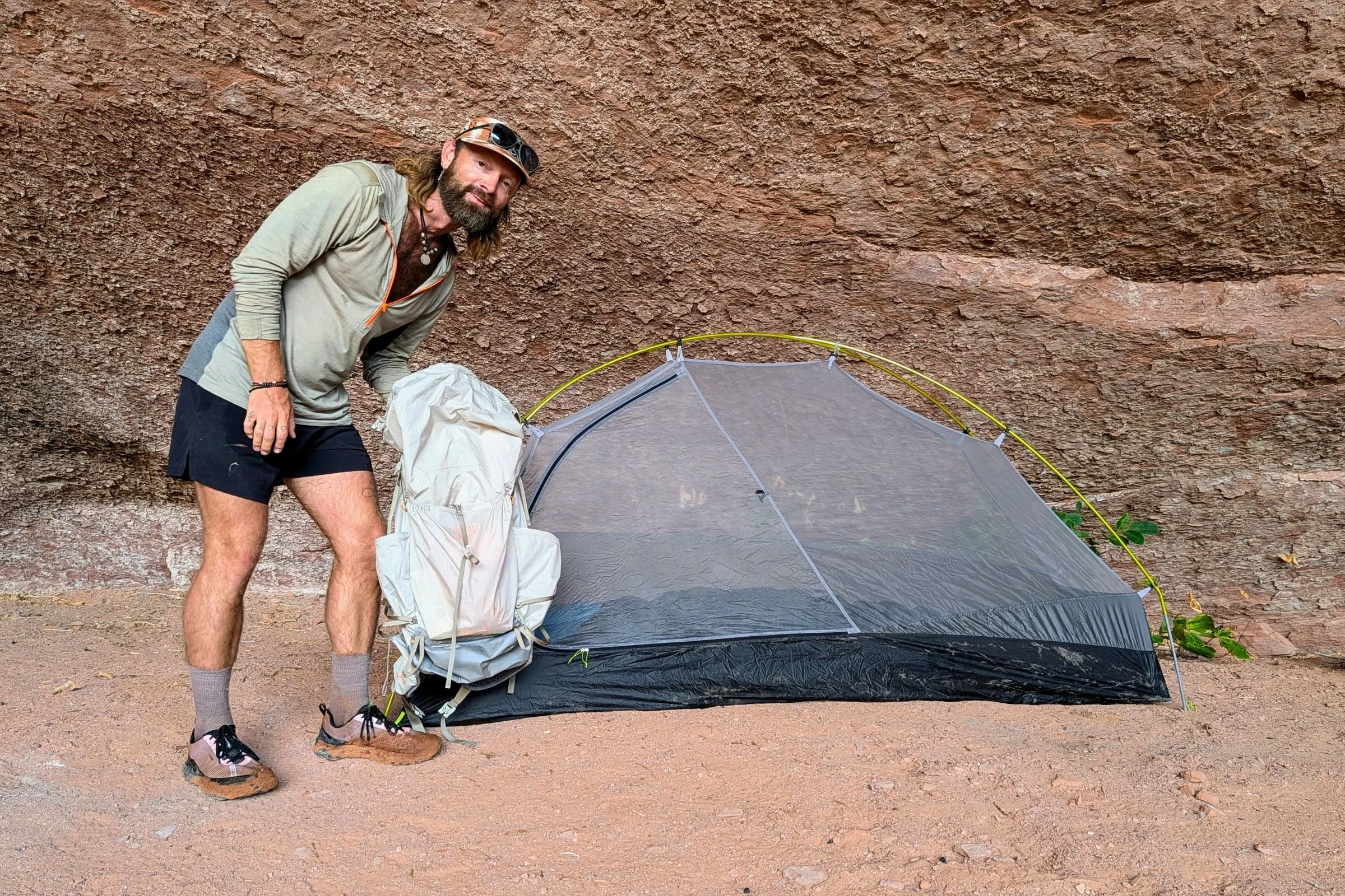 The author holds a backpack beside the Gossamer Gear The Free pitched without its rainfly against a rock wall.