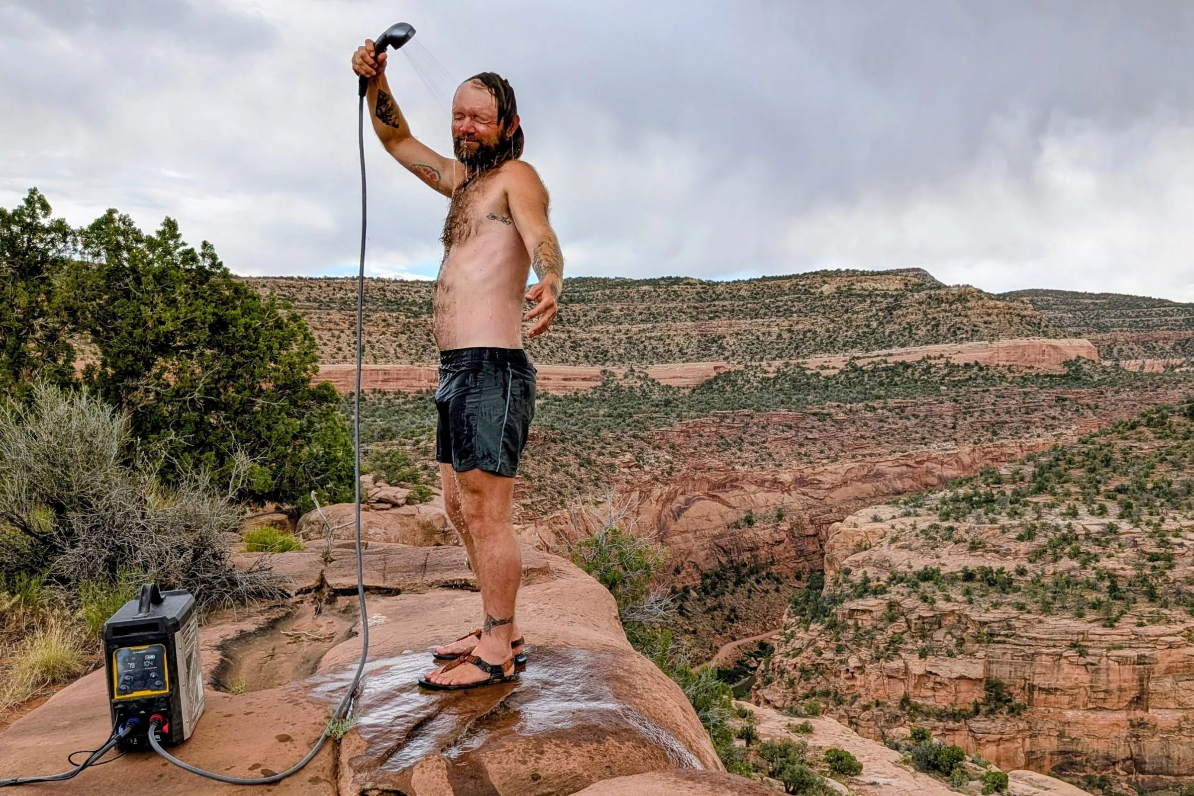 BougeRV Portable Propane Outdoor Water Heater outdoors near a shirtless person and a water hose.