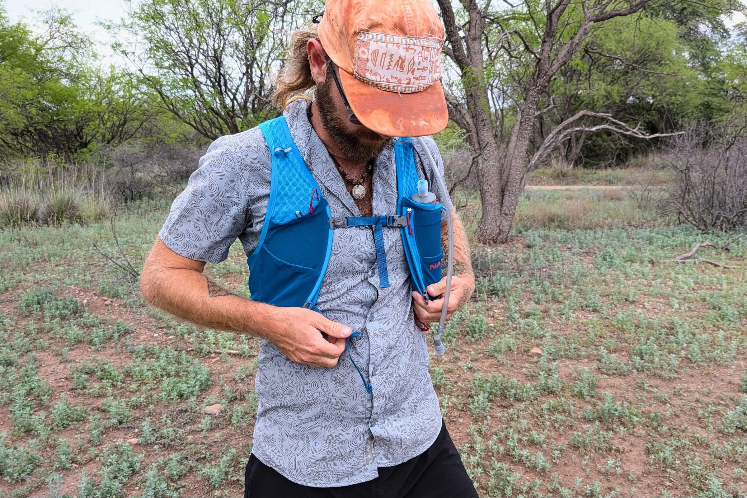 Man wearing a hat and Nathan VaporAir pack, standing in an open field with gear loaded.