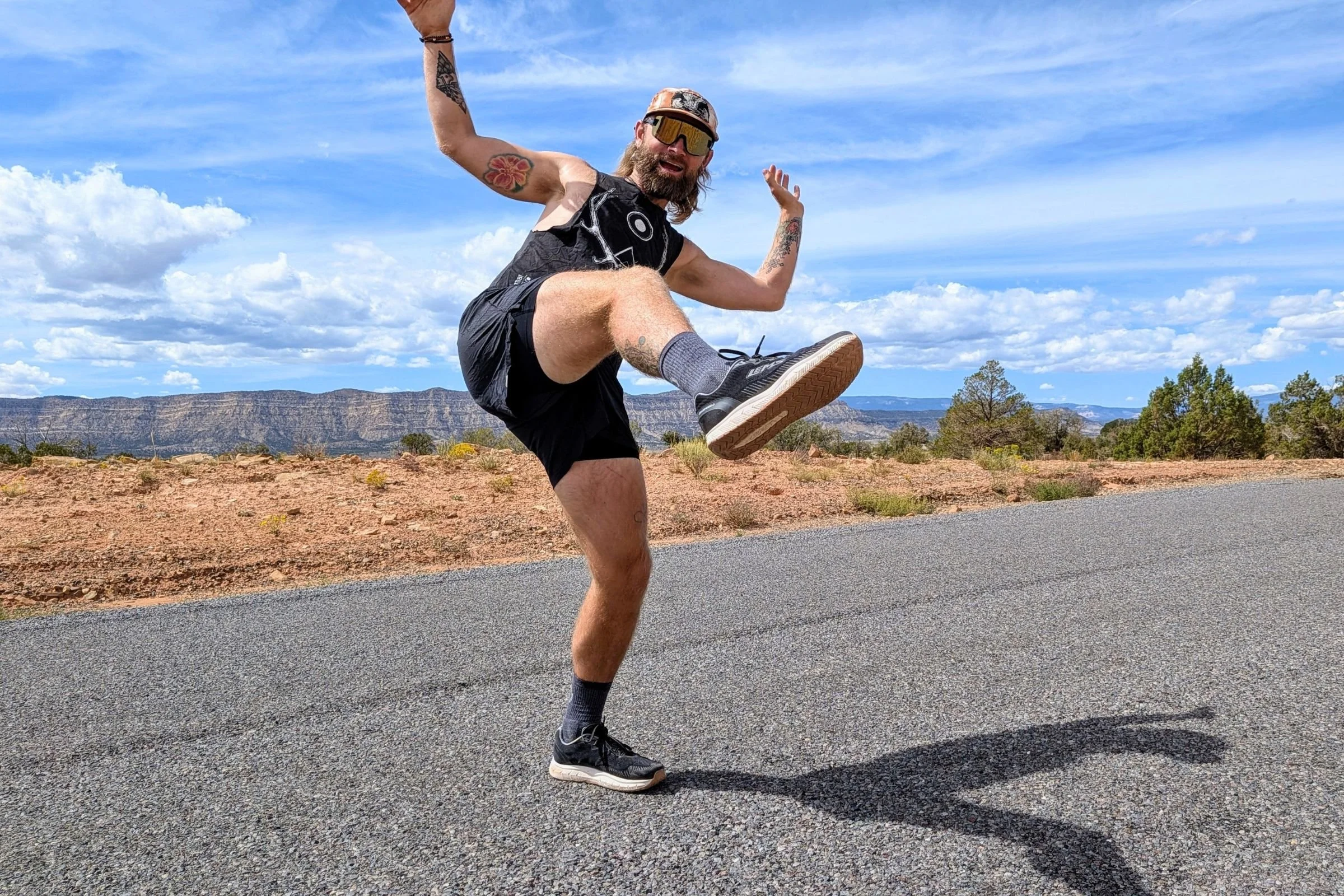 The author, Sam Schild, wearing shorts and a tank top while wearing the Lems ZENSPEED+ running shoes on a paved mountain road.