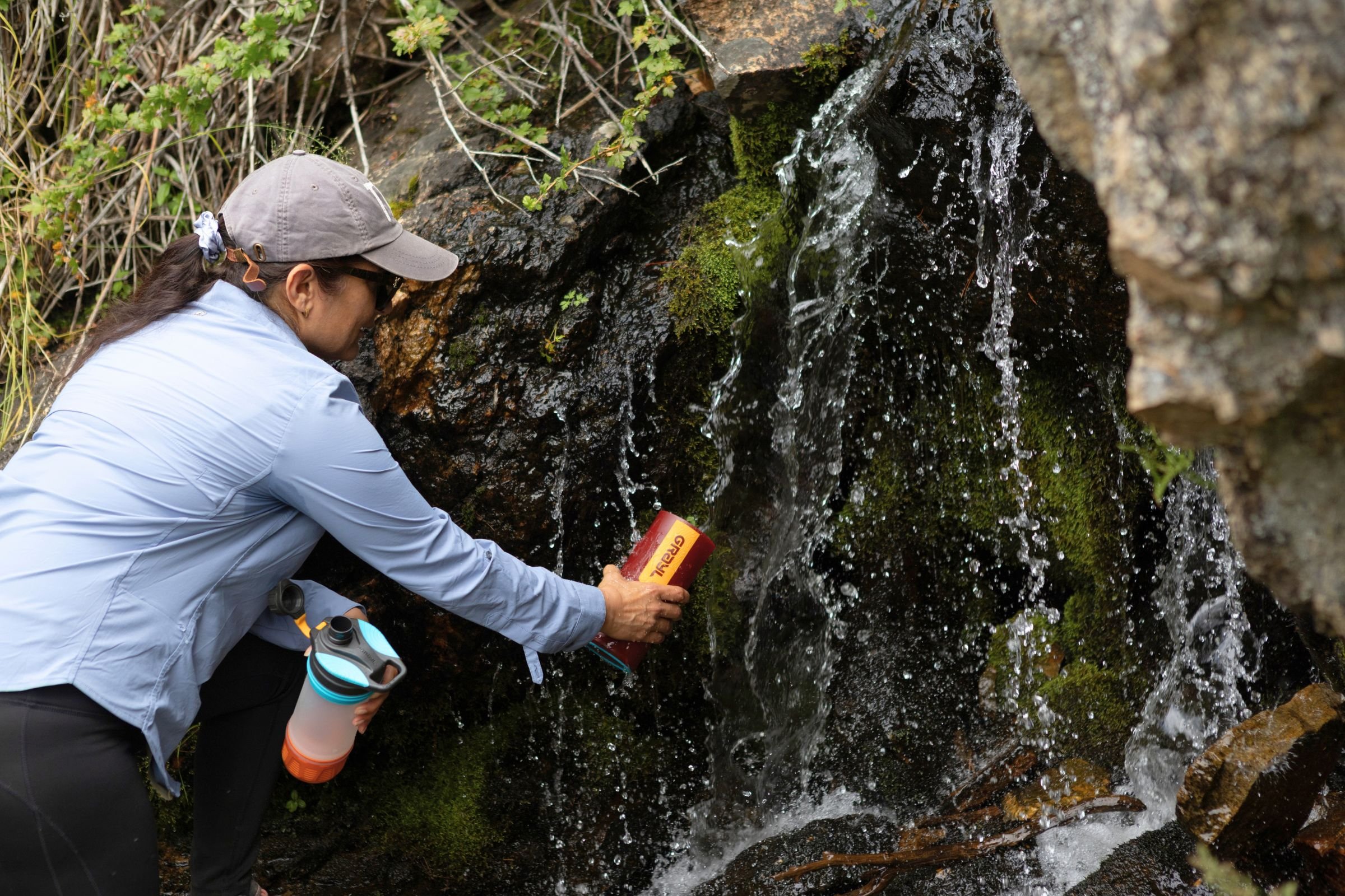 A woman filling a Grayl GeoPress Purifier from a waterfall.