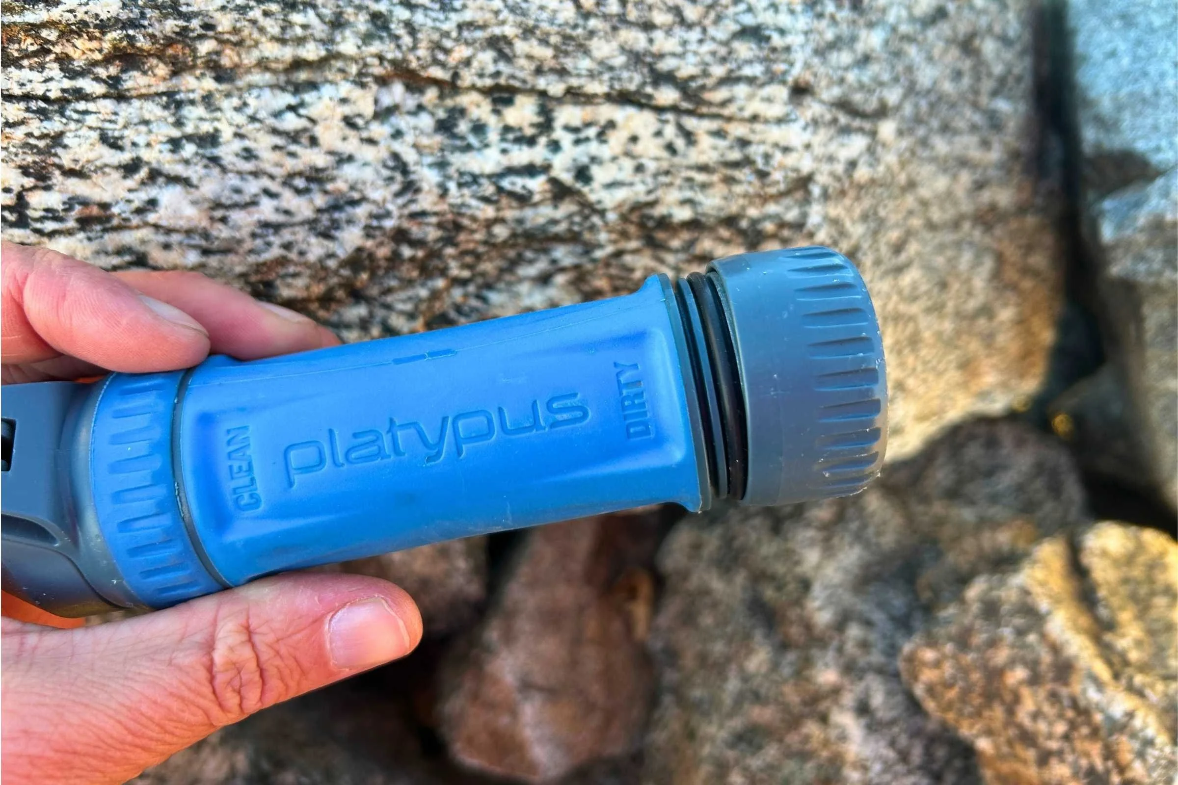 Platypus QuickDraw water filter held over rocks, showing the clean and dirty end connections