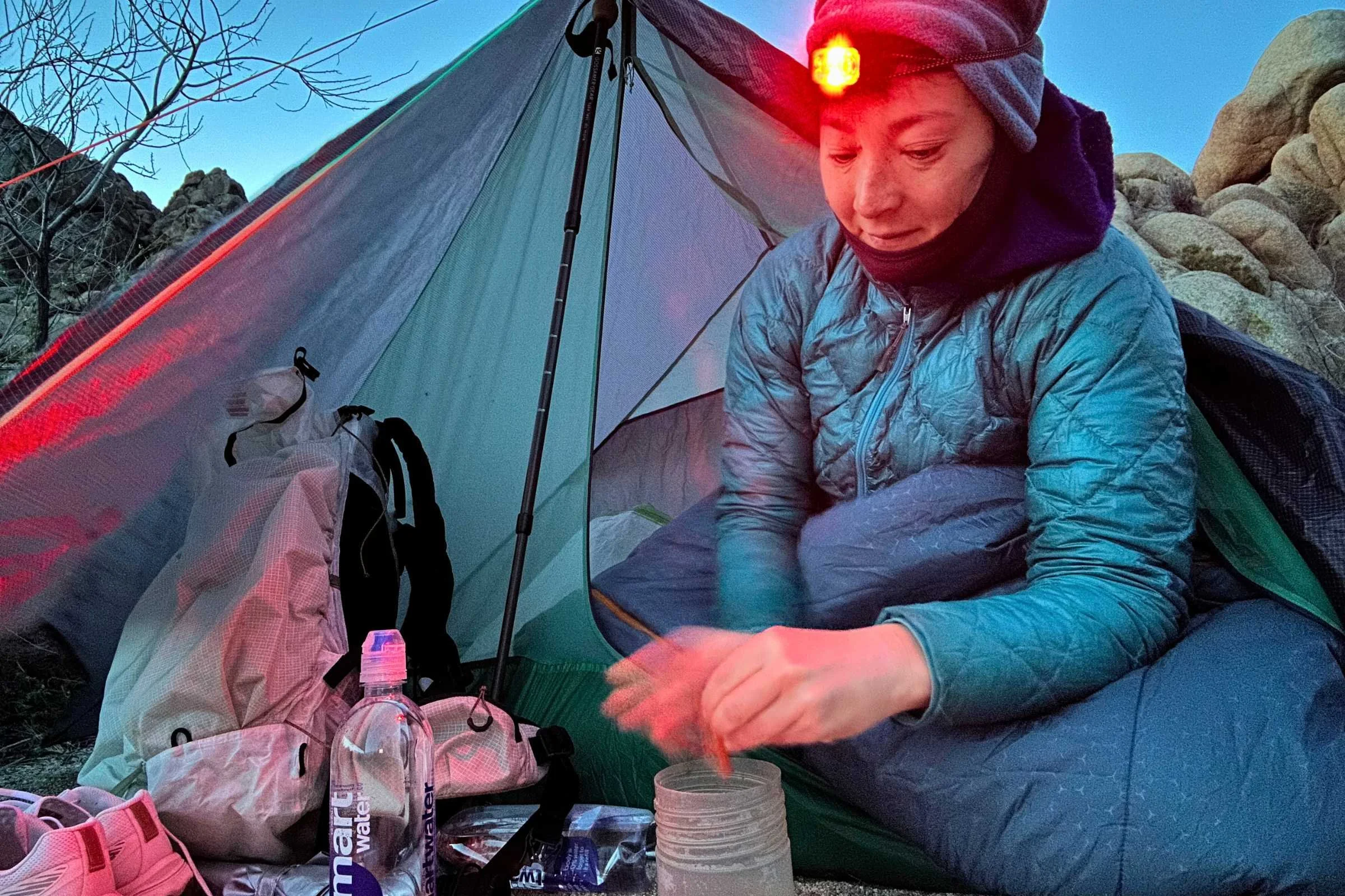 Backpacker using the red-light mode on the Nitecore NU25 MCT headlamp while preparing food in vestibule while bundled up inside a tent at dawn.
