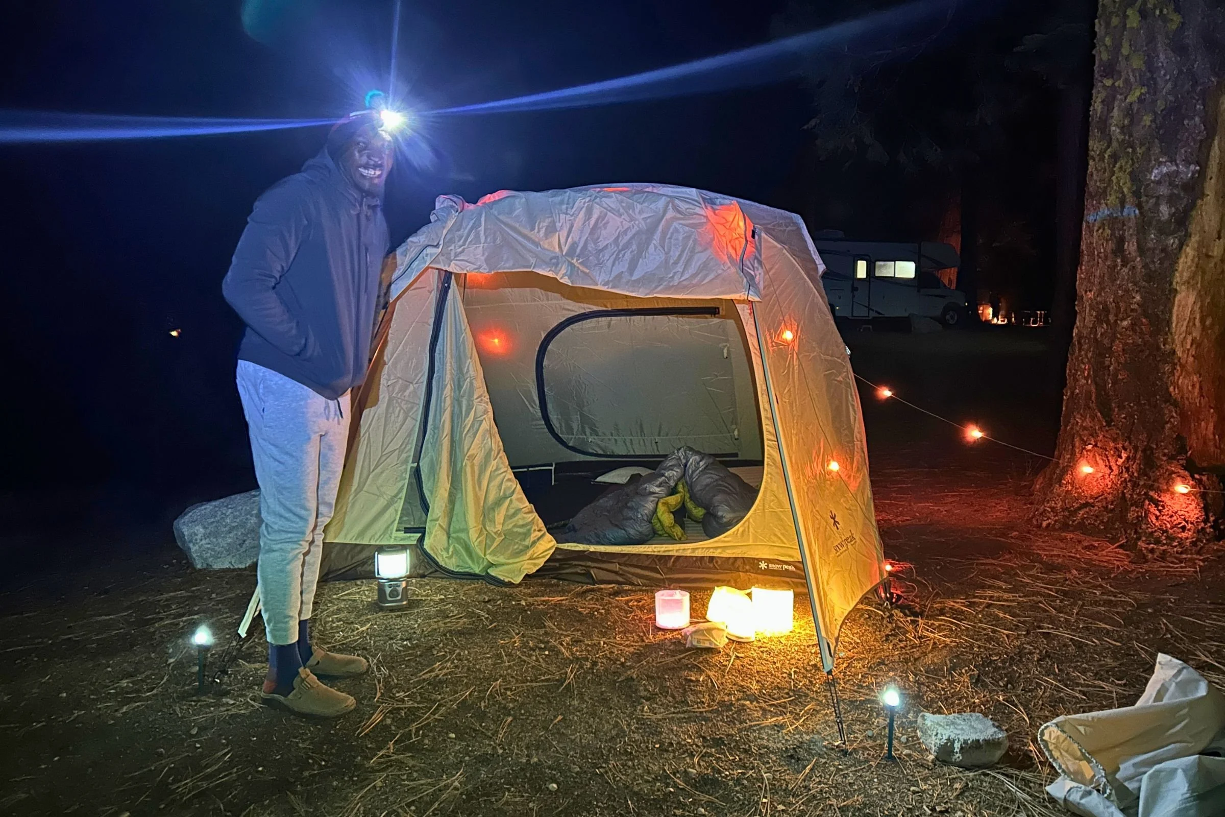 A tester stands beside a tent decorated with BioLite Luci 44' Solar String Lights at night.
