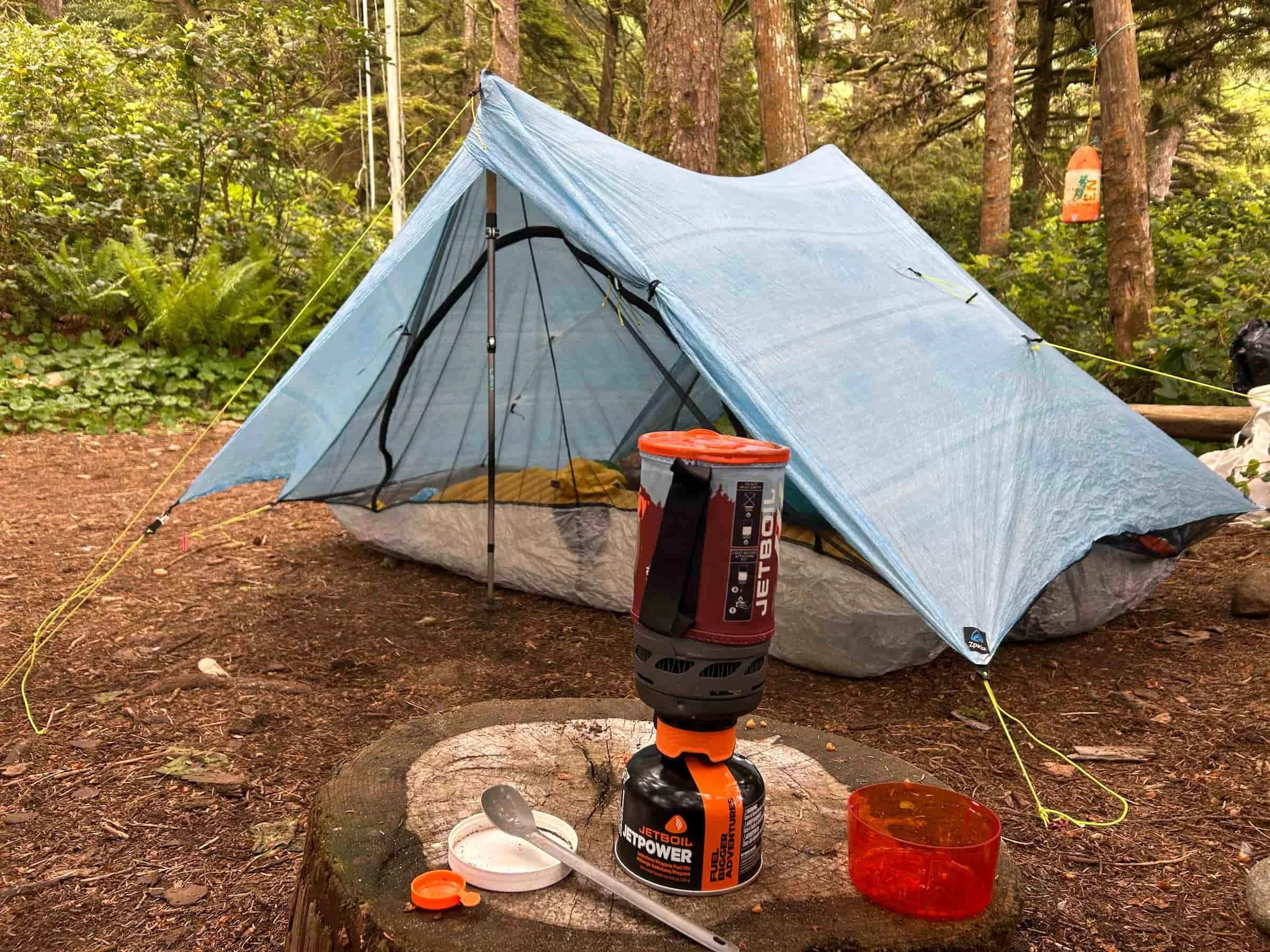 blue lightweight tent set up with a jetboil flash backpacking stove in the foreground on a stump