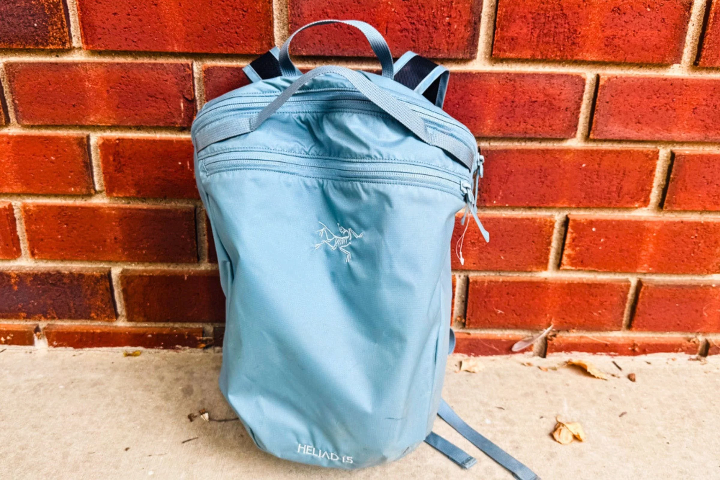 Blue Arc’teryx Heliad 15 backpack standing against a brick wall.