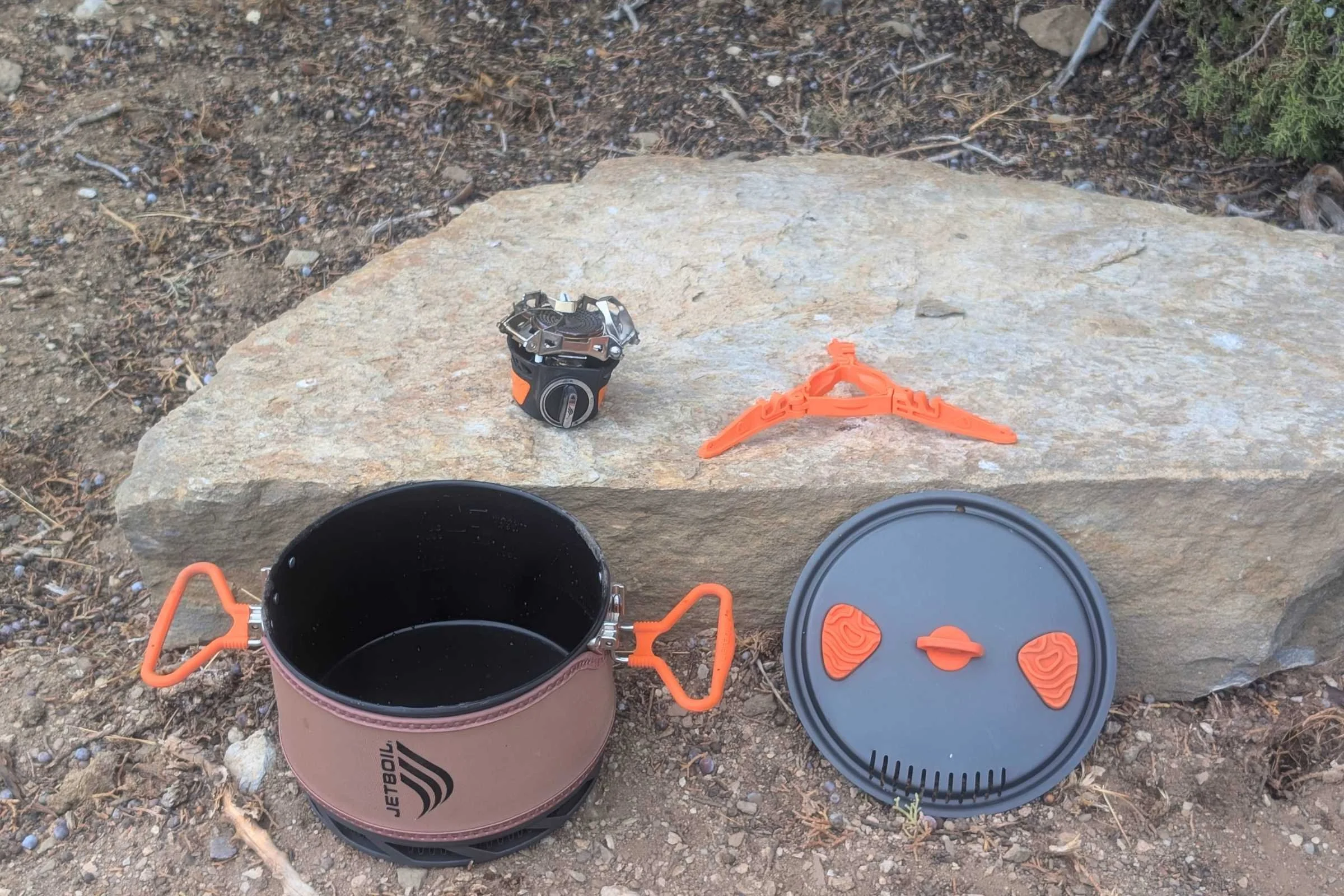 All items included with the TrailCook 2.0l laid out on a rock including the pot, pot lid, plastic base, and burner.
