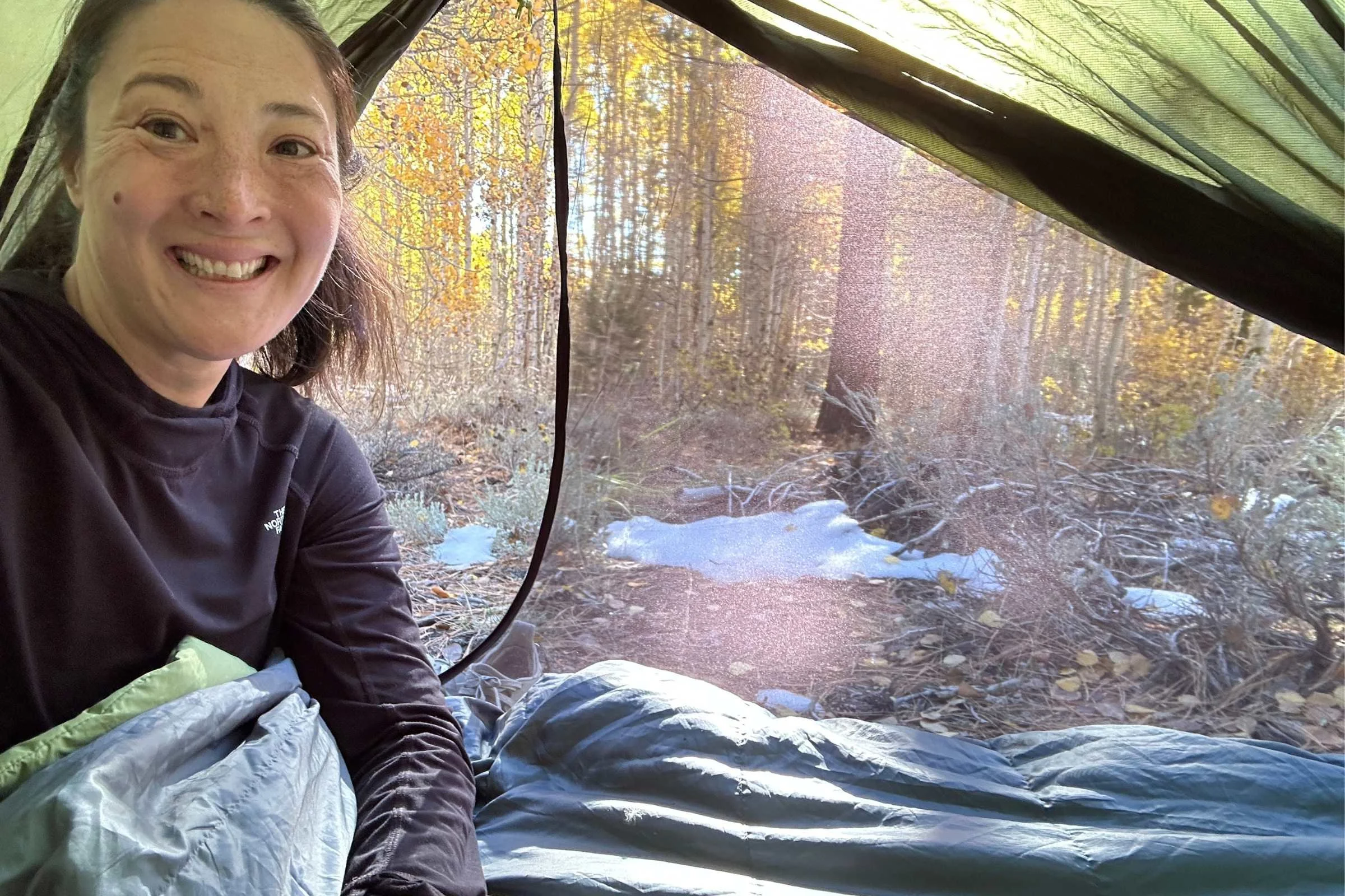 Camper inside tent using REI HunkerDown sleeping bag during chilly fall morning camping test