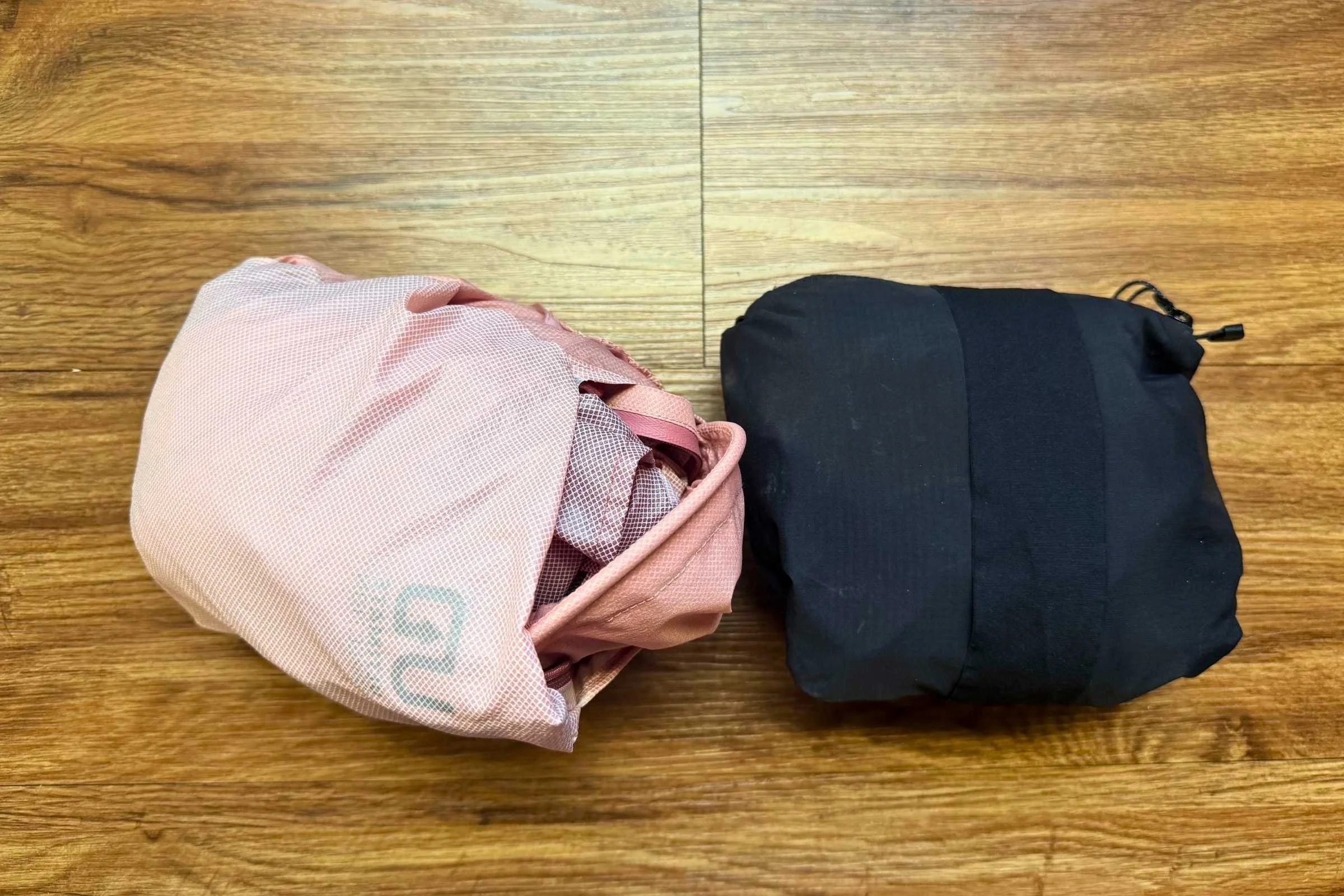   The Ultimate Direction Ultra Jacket (left) and Janji Rainrunner Pack Jacket 2.0 (right) pack down to about the same size, though the Janji Rainrunner zippers shut, ensuring it won’t bloom open, and has an arm band if you have nowhere to stow the ja
