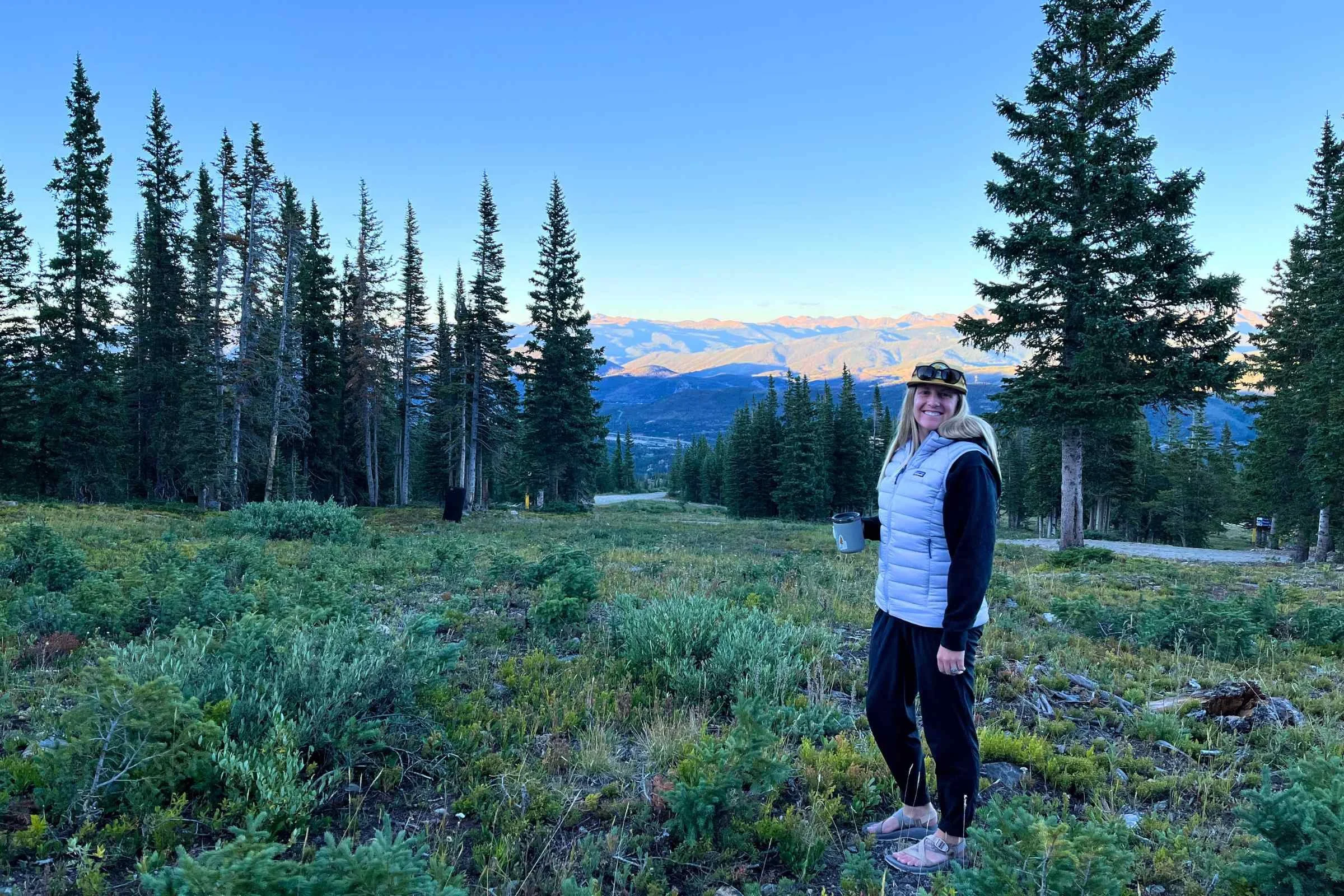   Woman standing in a field with Ponderosa Pines in the backgroun wearing a Patagonia Down Sweater Vest  