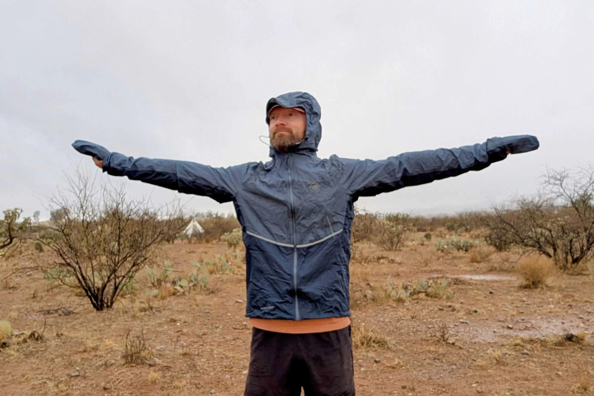   Man wearing an Ultimate Direction Ultra jacket with hood up and hand covers on with his arms spread wide  