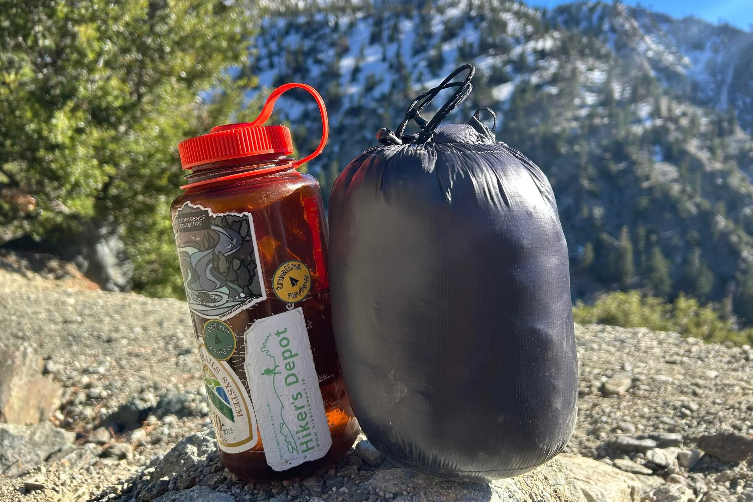   La Sportiva Lumina down jacket packed into compression sack showing compact size next to Nalgene bottle  