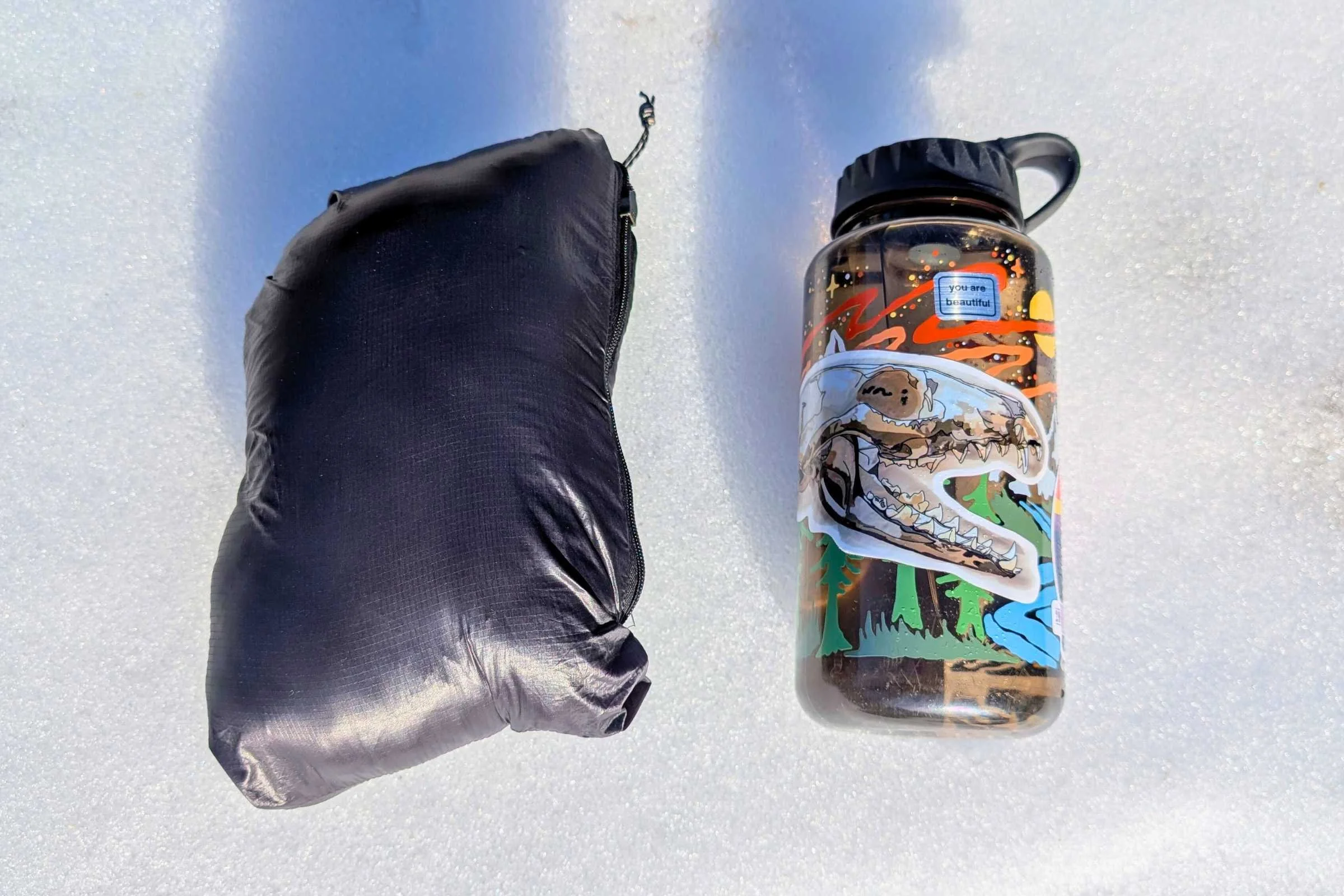   La Sportiva Lumina down jacket packed into compression sack showing compact size next to Nalgene bottle  