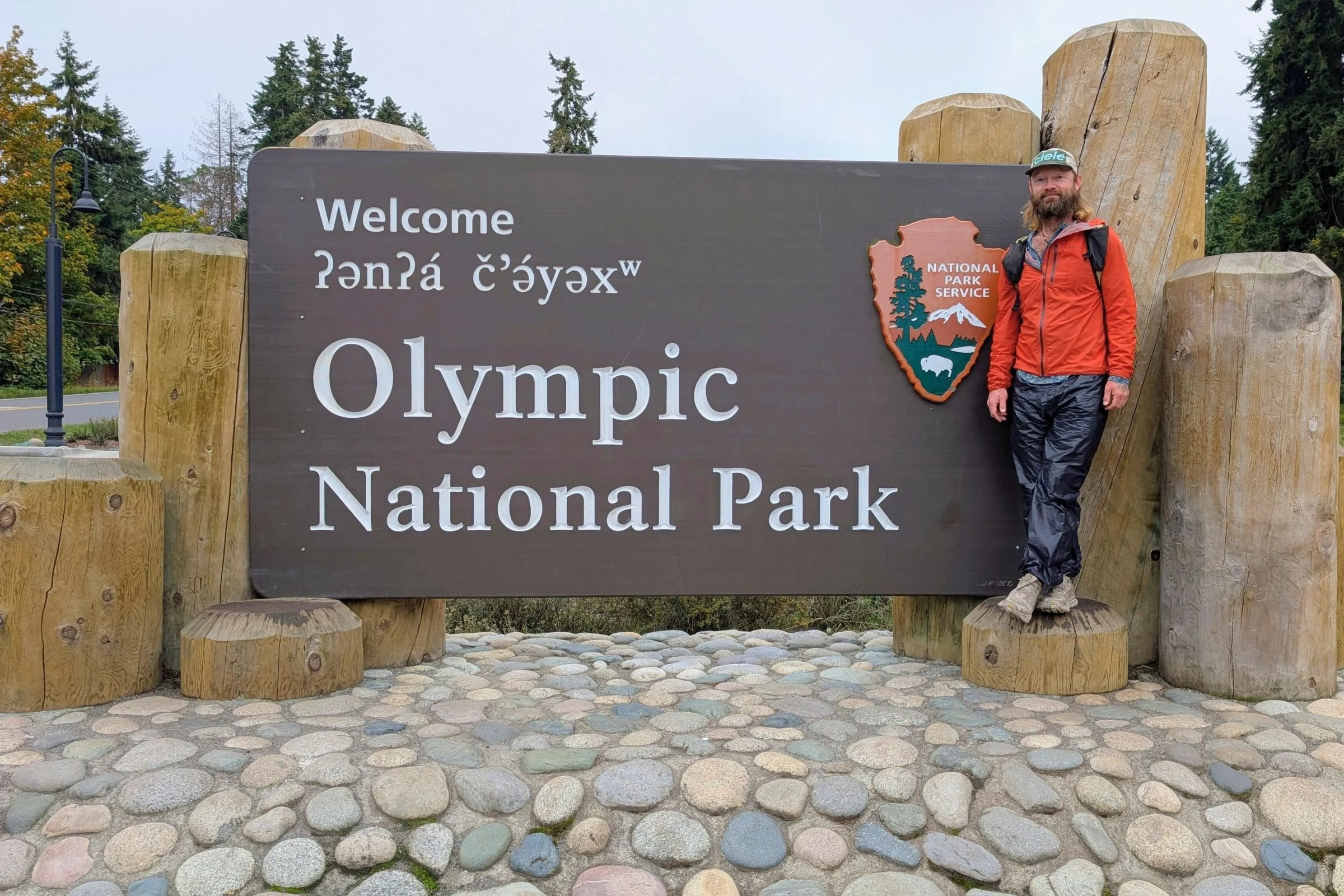   Man standing next to the Olympic National Park sign wearing the Altra Olympus 6  