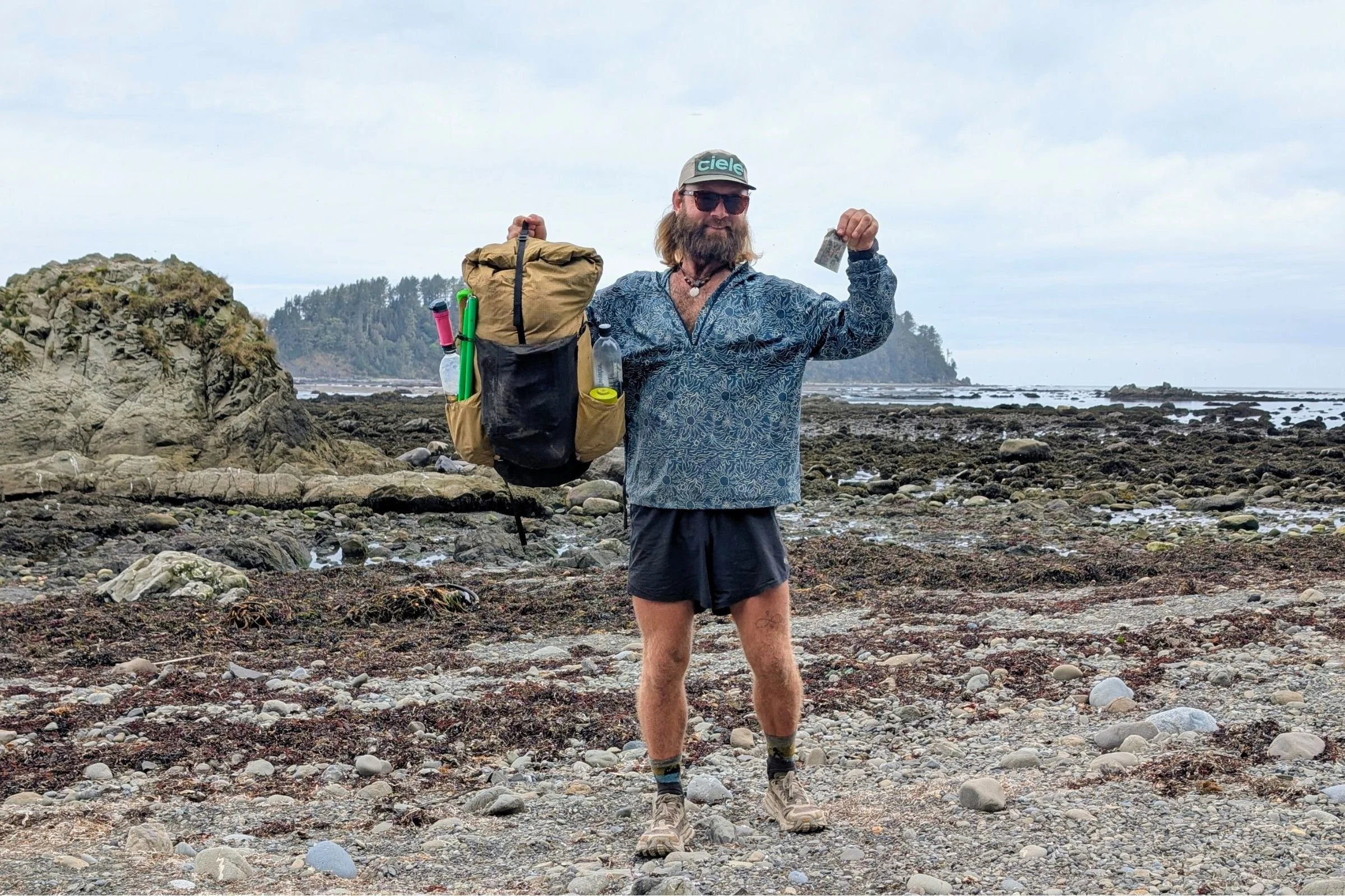   Man holding up an ultralight backpacking pack on the trail wearing the Altra Olympus 6  