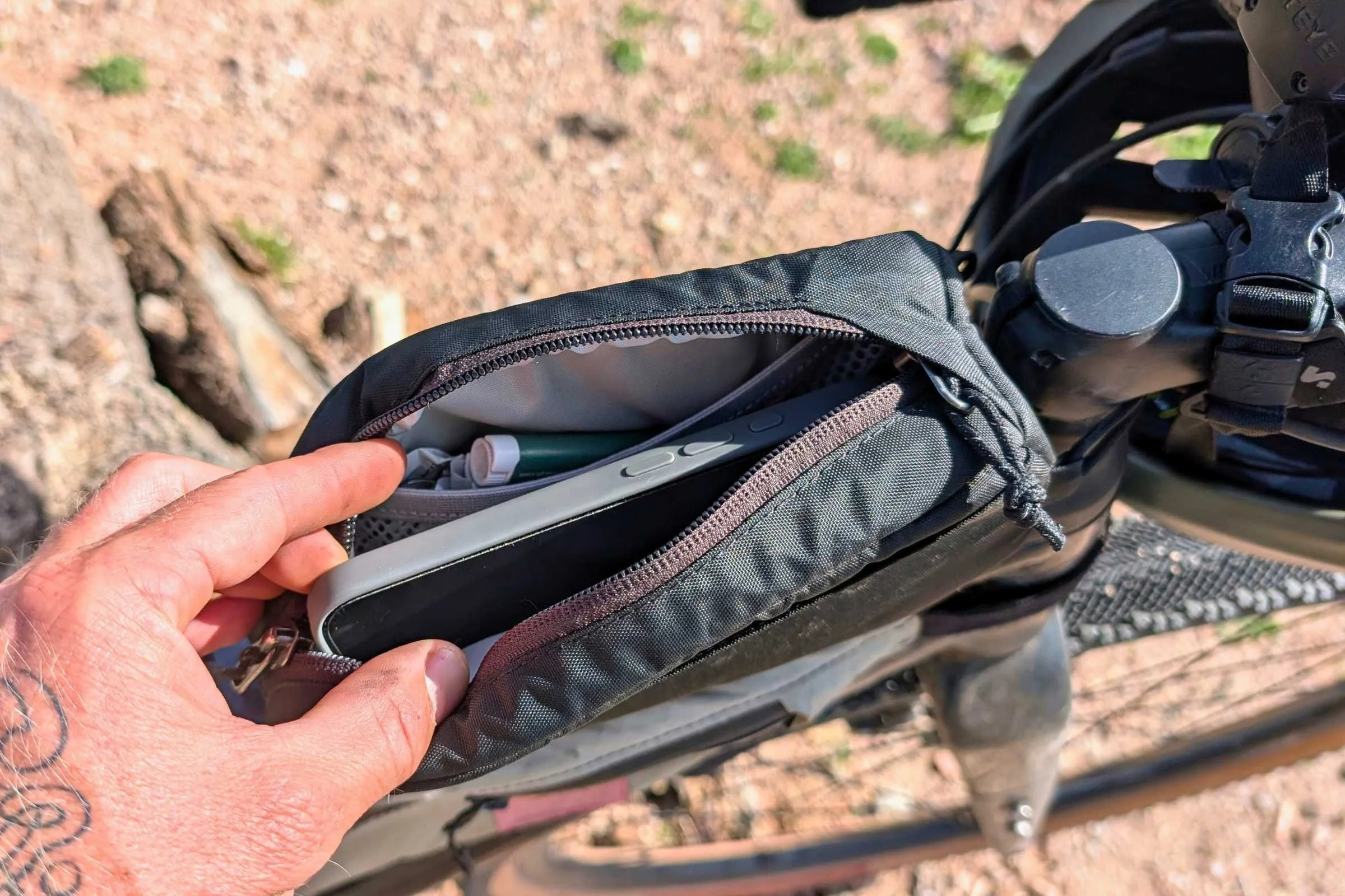   Hand opening the REI Co-op Junction Top Tube Bag on a bike to show the interior storage compartment.  