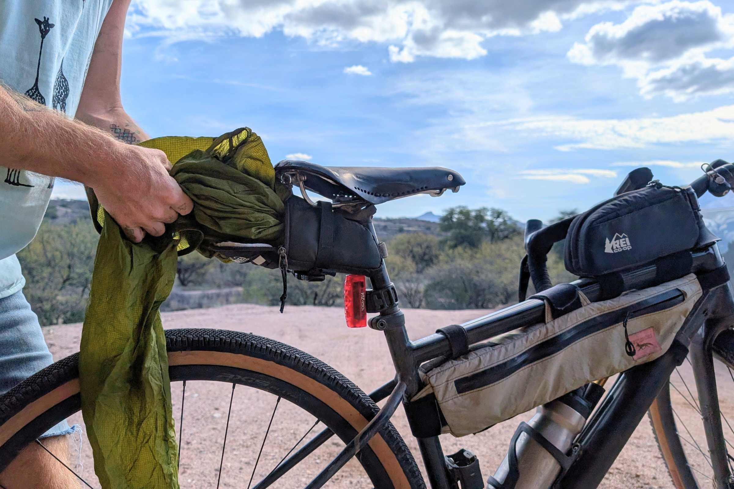   Person stuffing a green jacket into Junction Top Tube Bag behind the saddle on a gravel bike.  