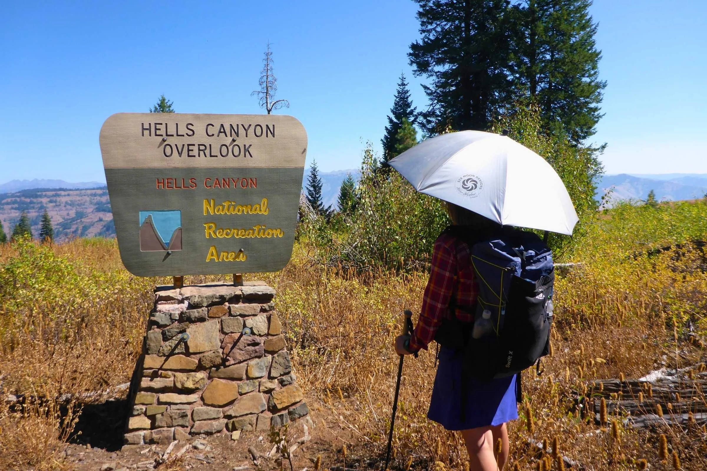   Hiker looking at a Hells Canyon Overlook sign while protecting themselves from the sun using the SMD Silver Carbon hiking umbrella   