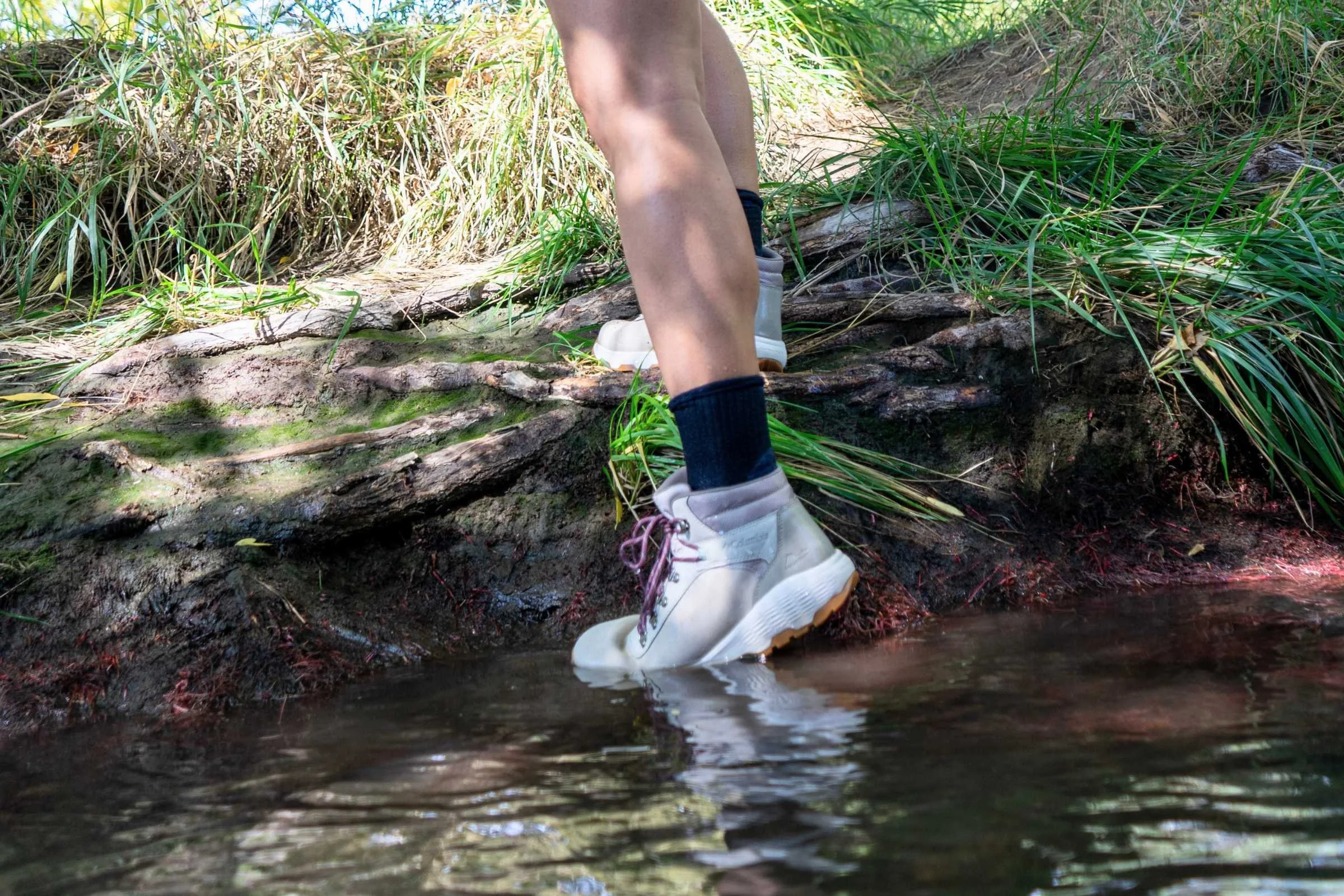   The Columbia Newton Wander hiking boots stepping into a shallow stream to demonstrate waterproof performance  