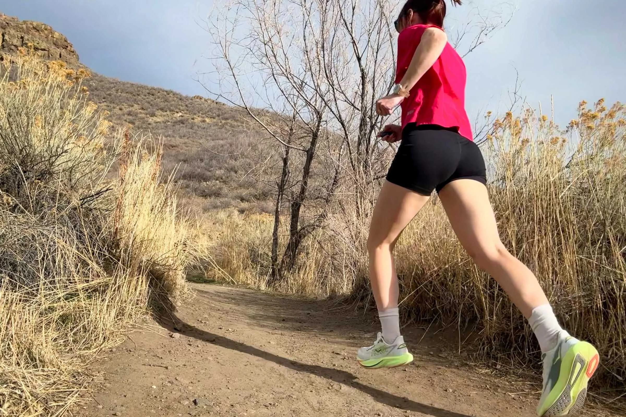   Woman running on a dirt trail wearing HOKA Mach 7 running shoes in a dry, grassy outdoor setting.  