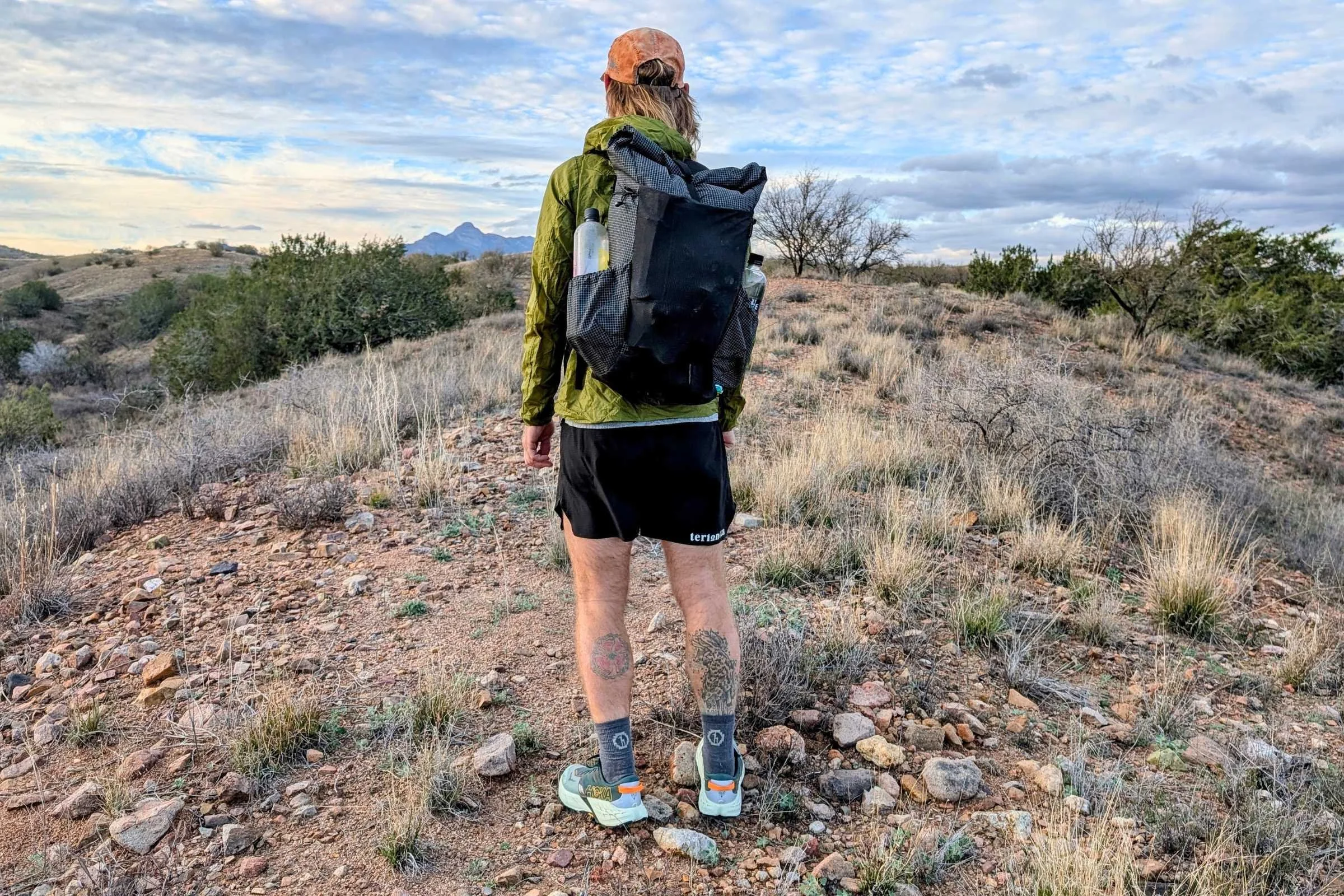   Rear view of a backpacker on rocky trail terrain wearing HOKA Speedgoat 7 trail running shoes with a pack.  