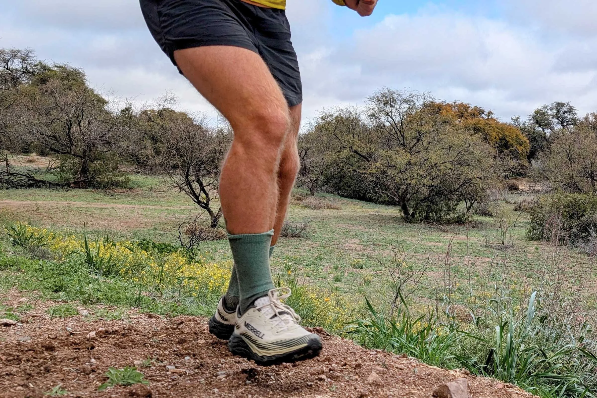   Close-up action shot of a runner wearing Merrell Agility Peak 6 trail running shoes on dirt trail terrain.  