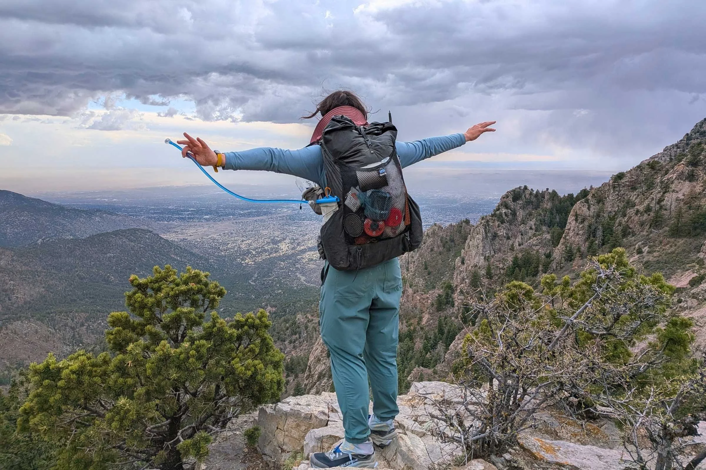   Rear view of a hiker on a mountain overlook wearing REI Trailmade Pull-On pants with arms outstretched.  