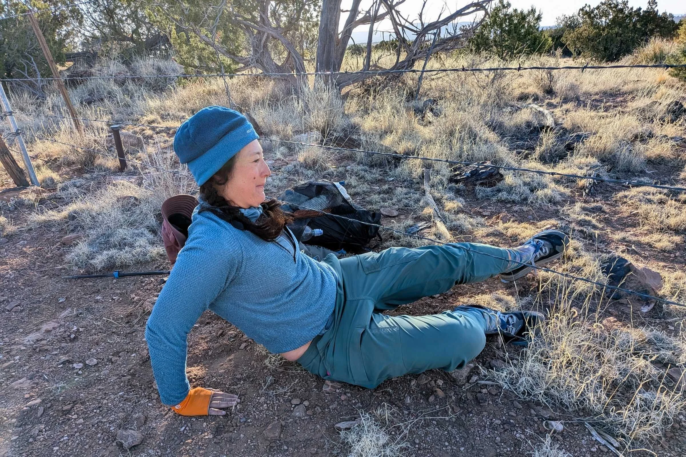   Hiker sliding under a low barbed wire fence wearing REI Trailmade Pull-On pants.  